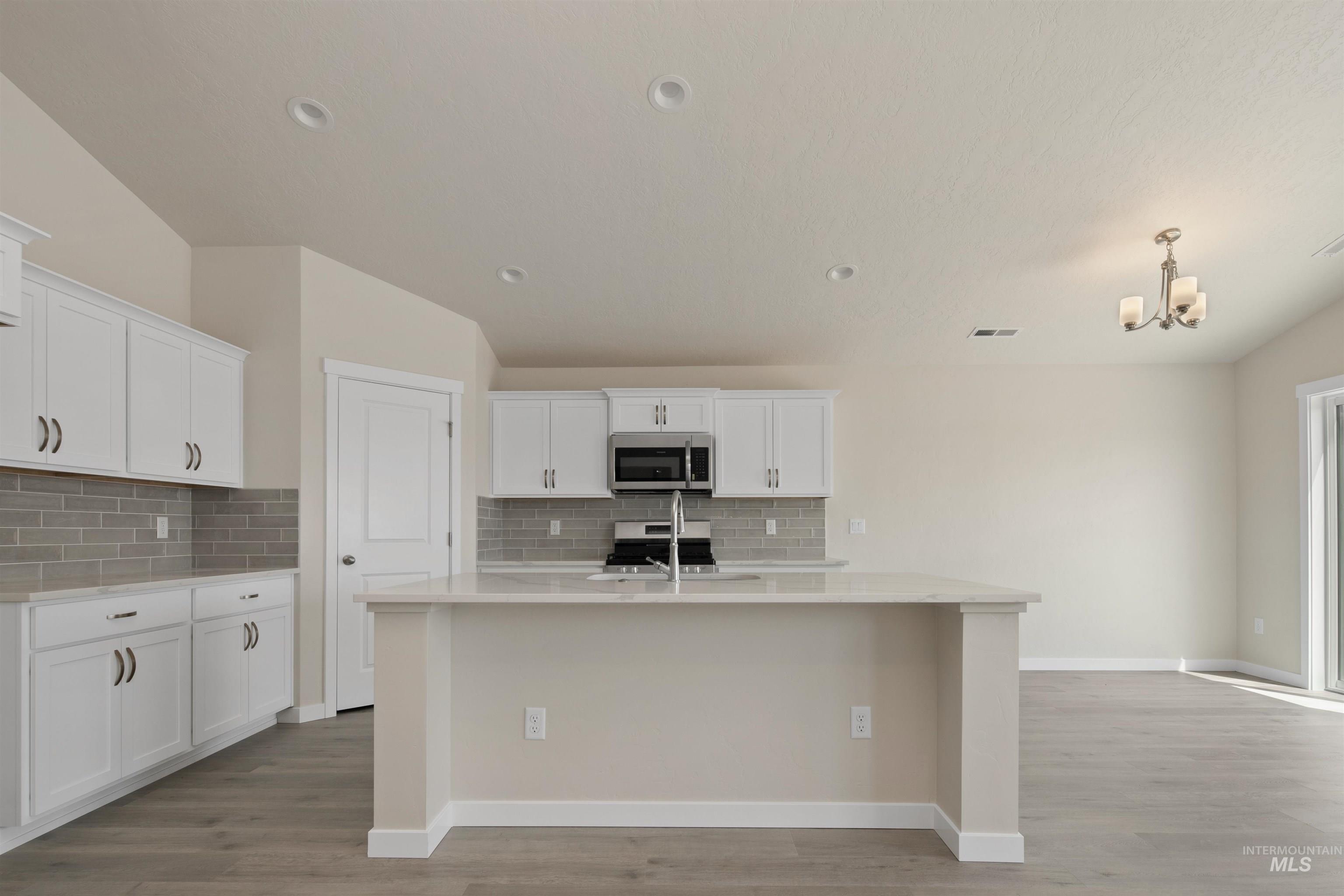 Kitchen with white cabinets, tasteful backsplash, a center island with sink, light stone counters, and recessed lighting