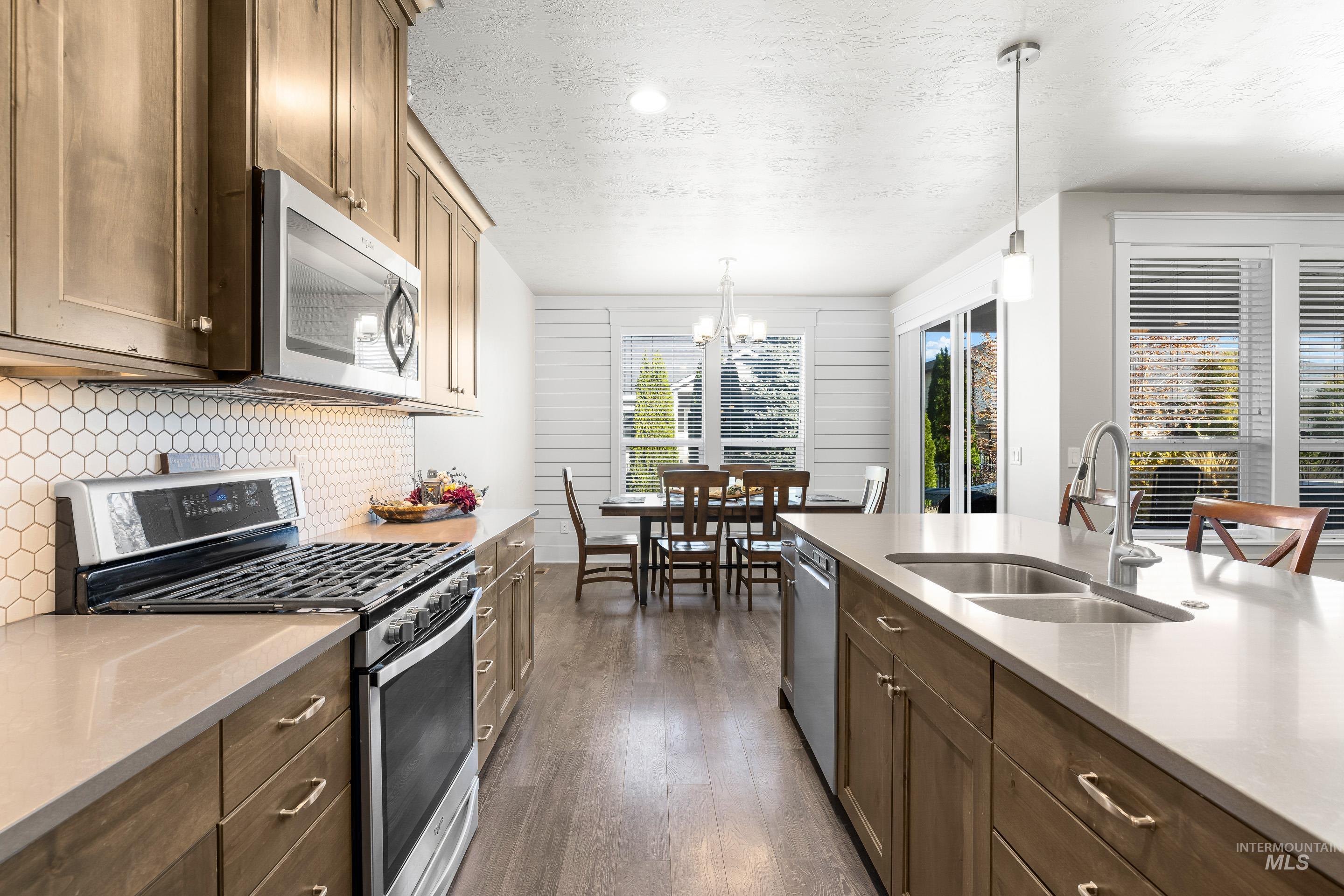 Kitchen with appliances with stainless steel finishes, light stone counters, a textured ceiling, dark wood-style floors, and hanging light fixtures