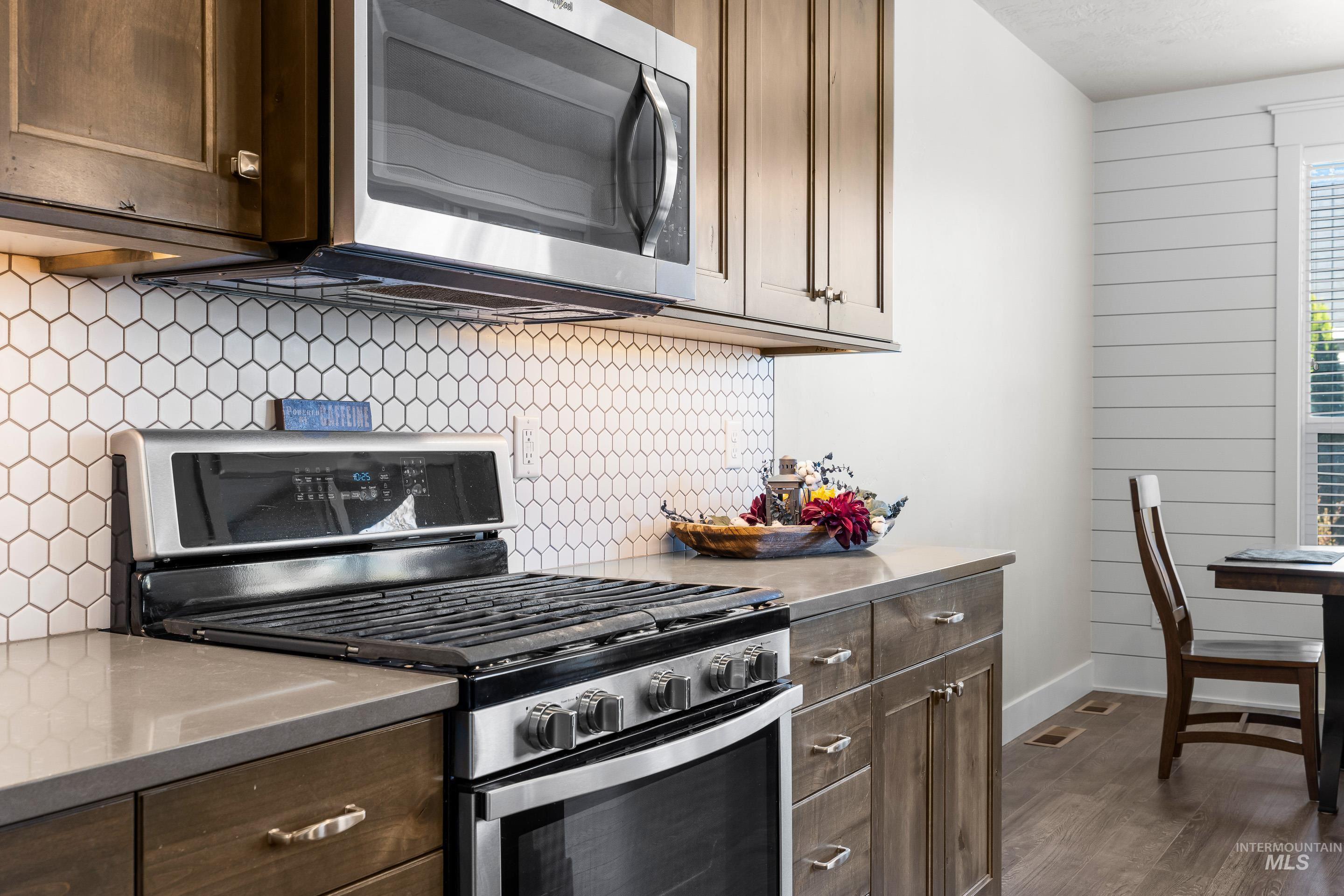 Kitchen featuring appliances with stainless steel finishes, backsplash, dark brown cabinets, dark wood-type flooring, and stainless steel countertops