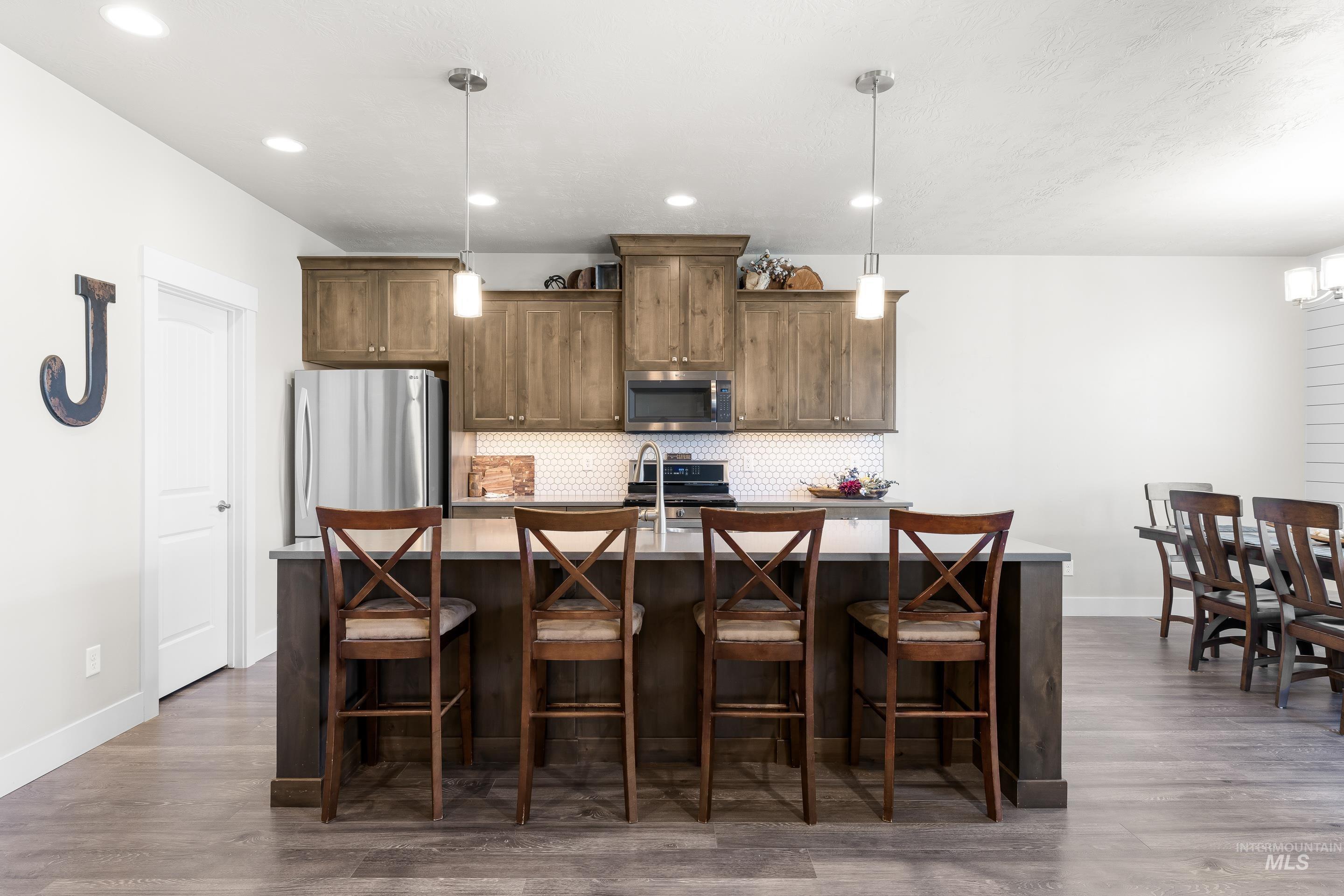 Kitchen with stainless steel appliances, a breakfast bar, hanging light fixtures, tasteful backsplash, and a center island with sink