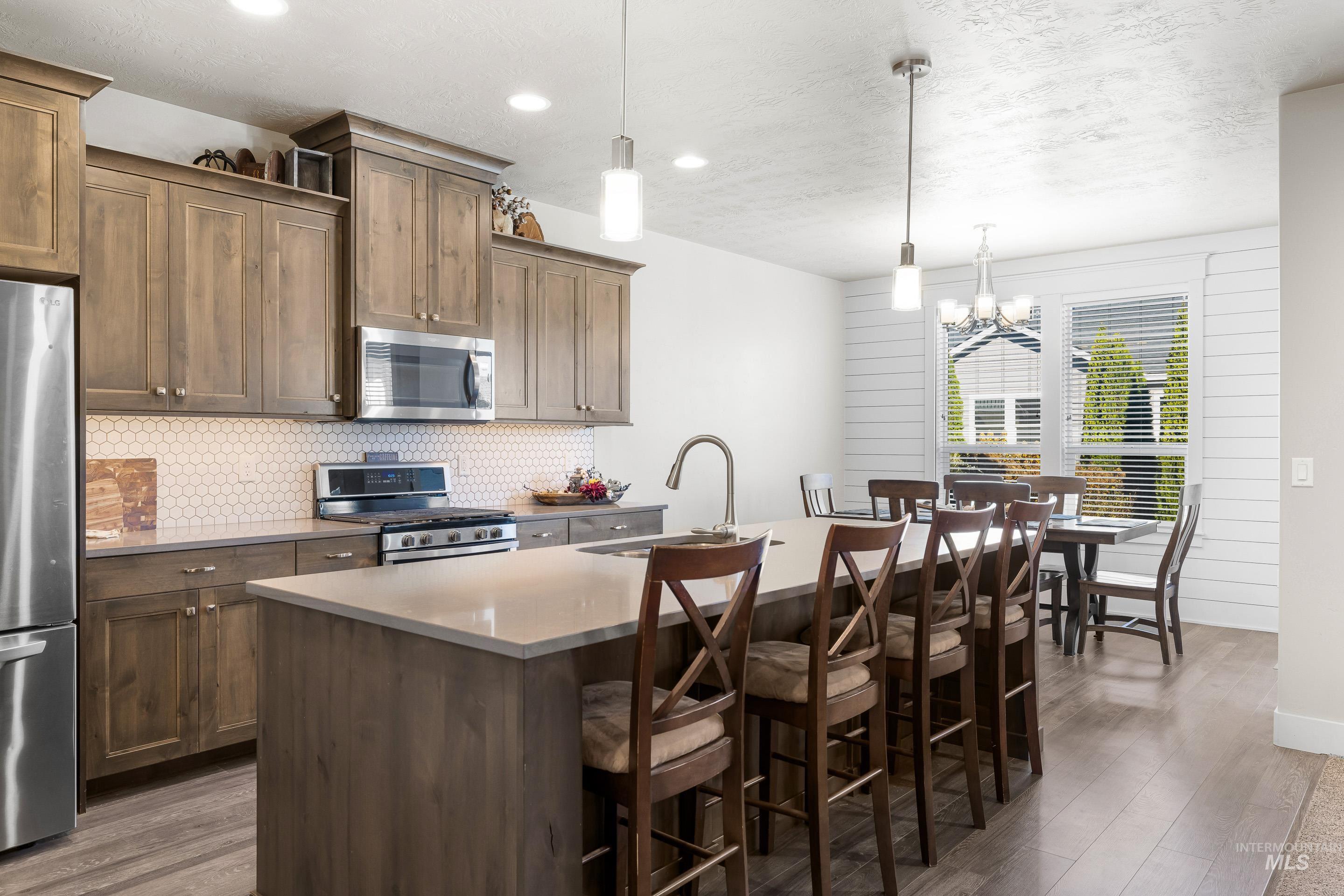 Kitchen with dark wood-style floors, stainless steel appliances, decorative backsplash, a kitchen island with sink, and recessed lighting