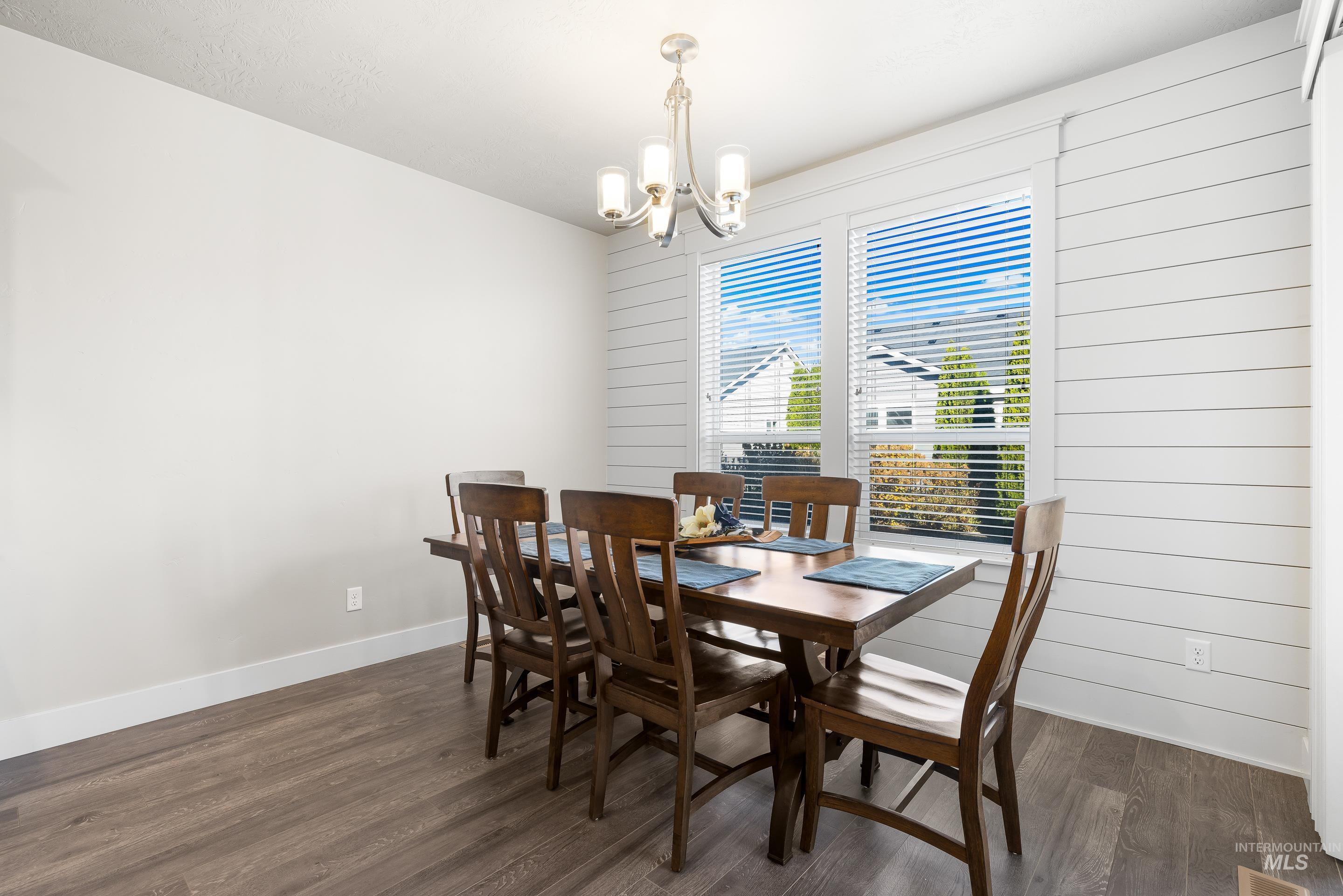 Dining space featuring dark wood finished floors, a chandelier, and wood walls