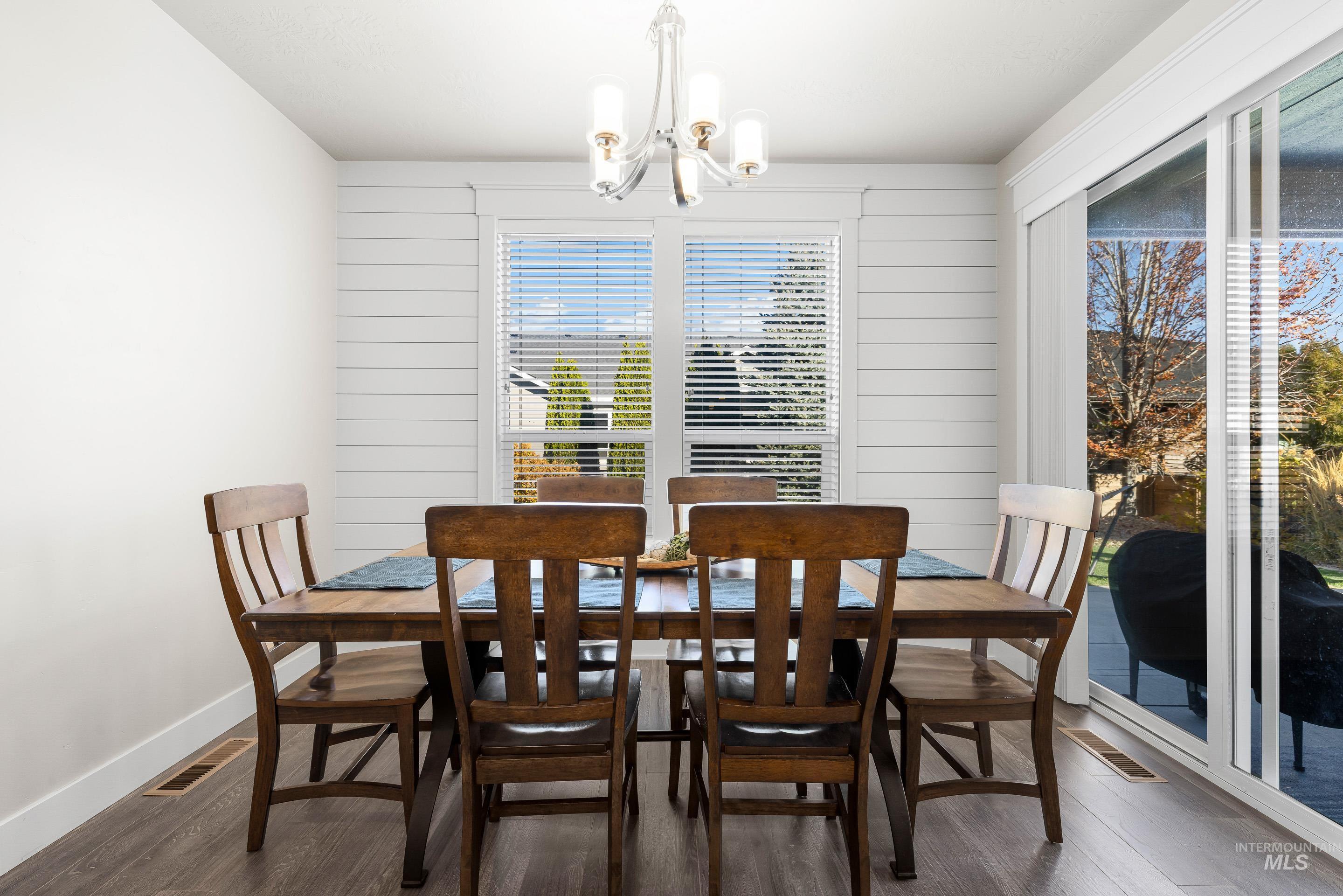 Dining room with dark wood finished floors, wood walls, and a chandelier