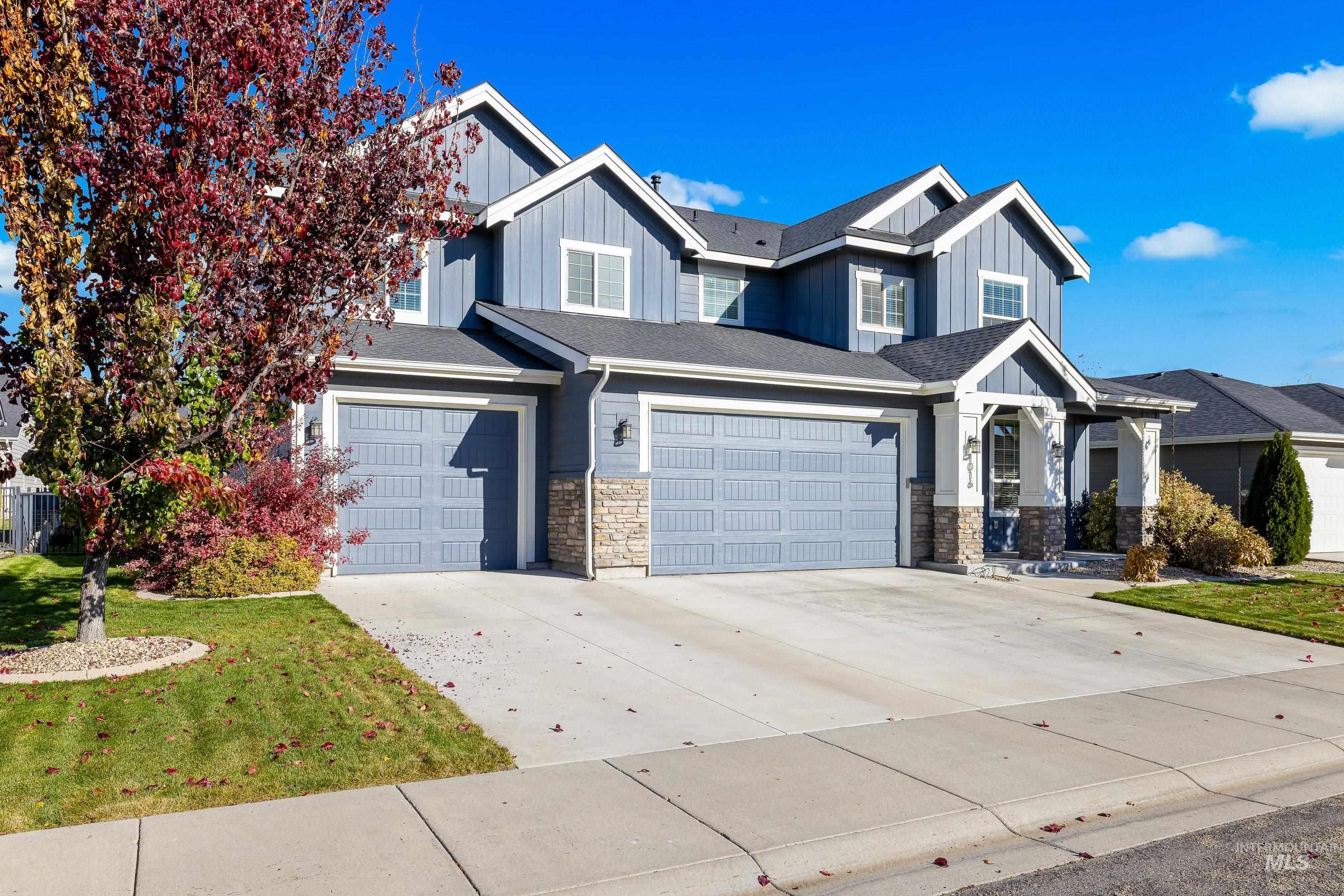 Craftsman-style home with board and batten siding, stone siding, driveway, a front lawn, and a garage