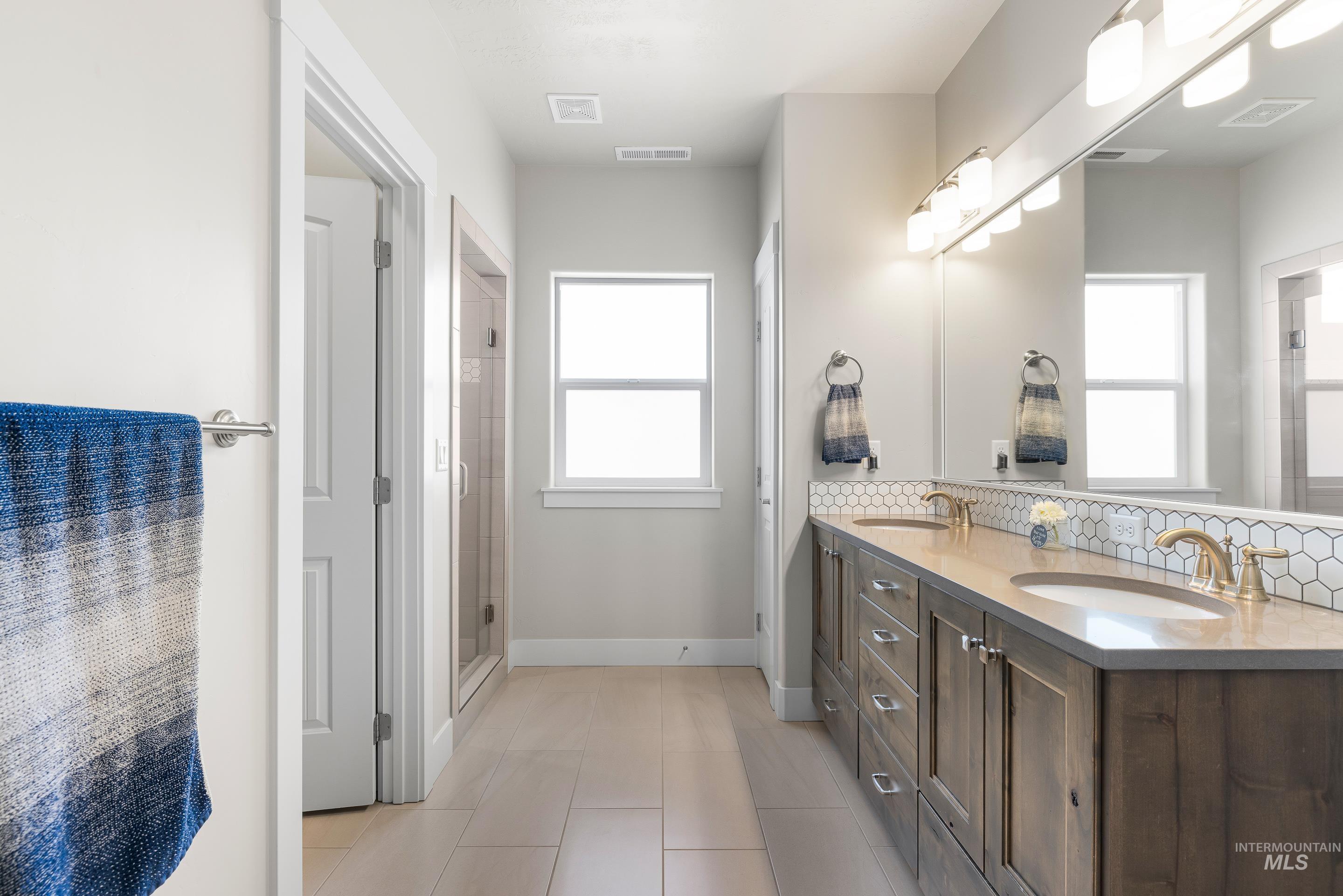 Bathroom with double vanity, plenty of natural light, light tile patterned floors, and a stall shower