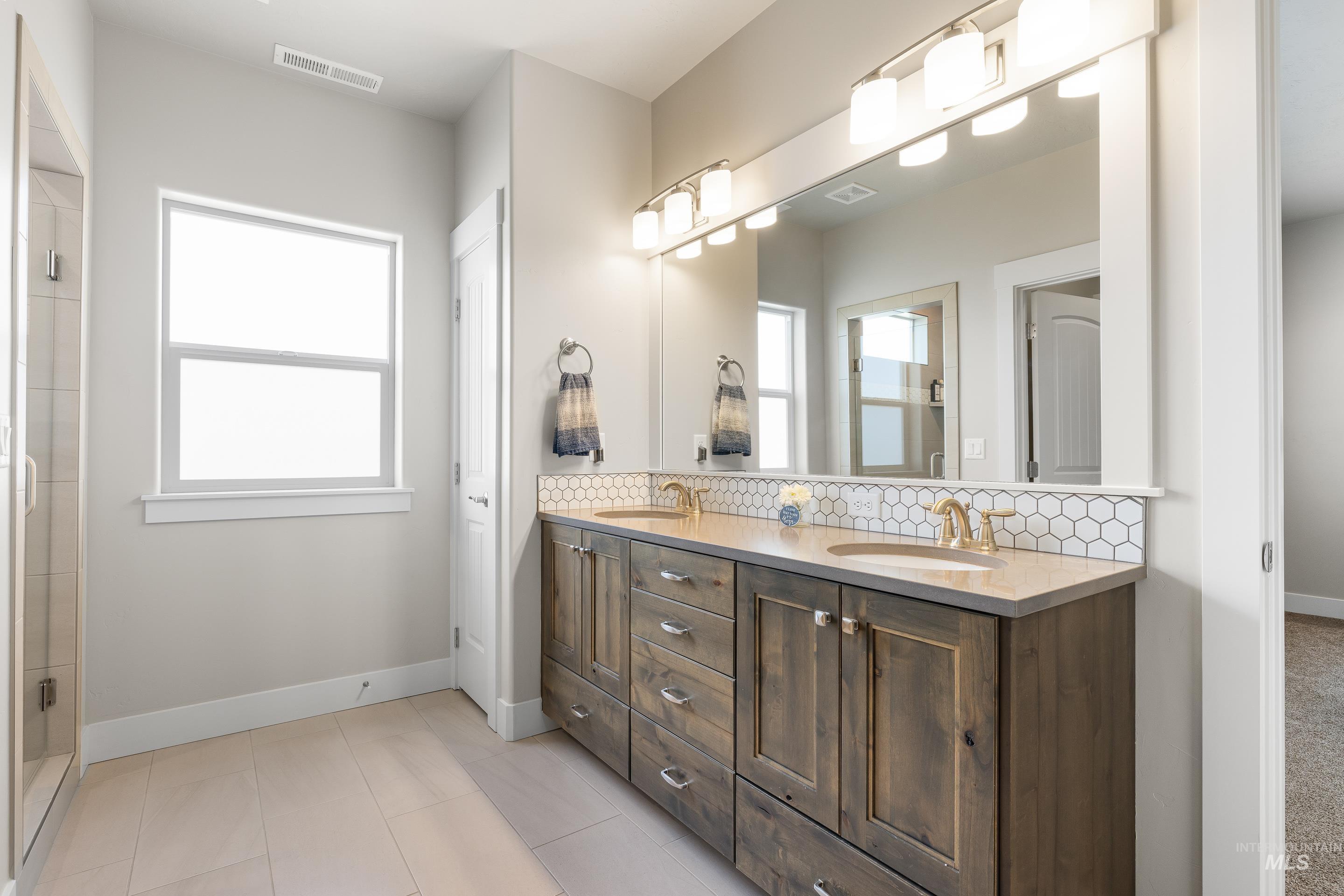 Bathroom with backsplash, double vanity, light tile patterned flooring, and a tile shower