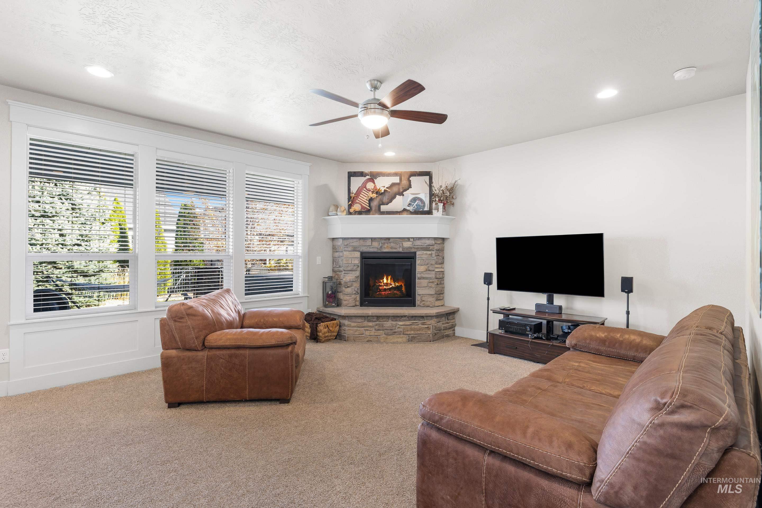 Living area with carpet, ceiling fan, a stone fireplace, and recessed lighting
