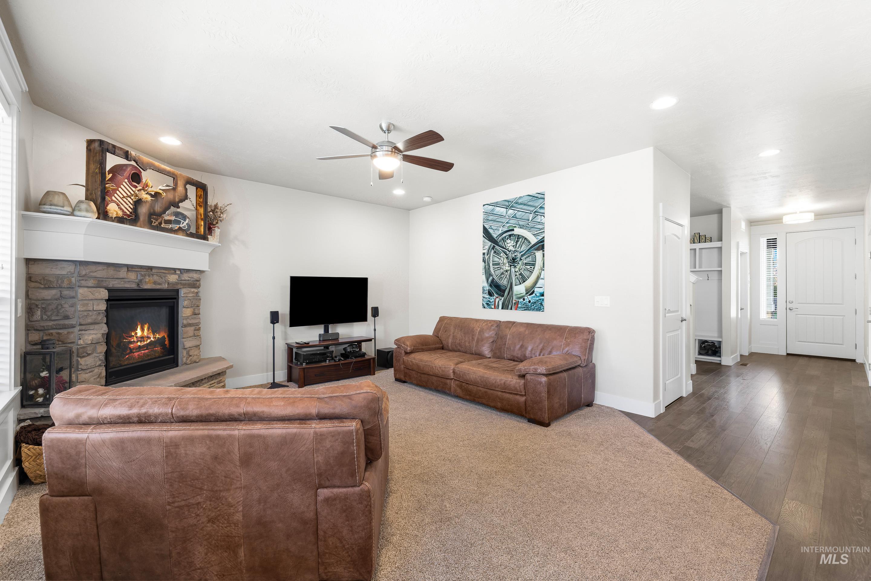Carpeted living area featuring a stone fireplace, a ceiling fan, recessed lighting, and wood finished floors