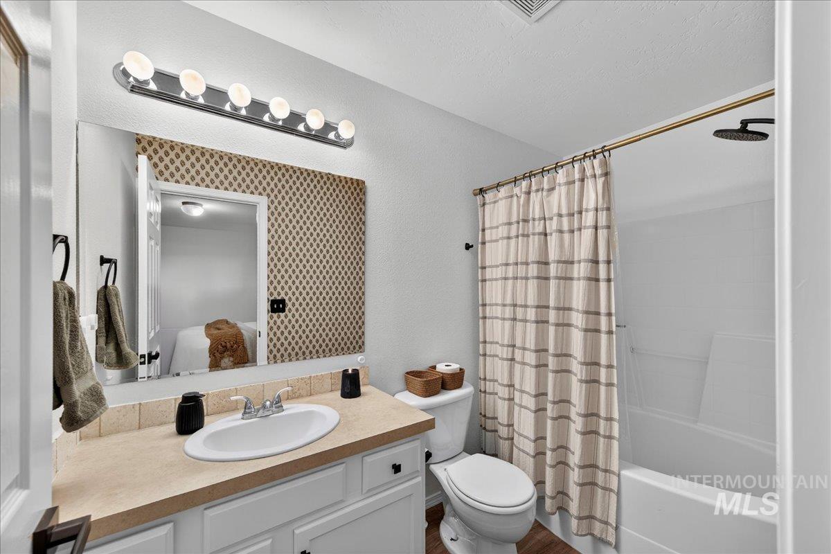 Ensuite bathroom with shower / bath combo with shower curtain, vanity, and a textured wall