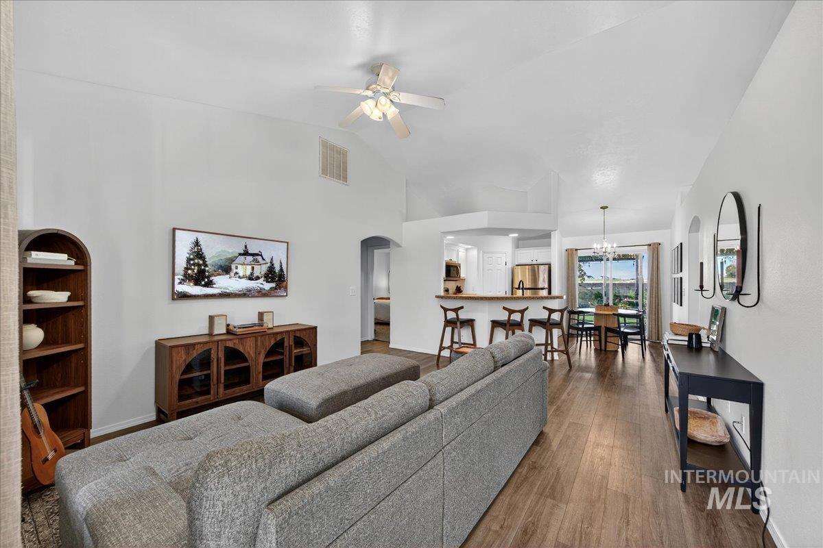 Living room featuring arched walkways, dark wood finished floors, ceiling fan, a chandelier, and high vaulted ceiling