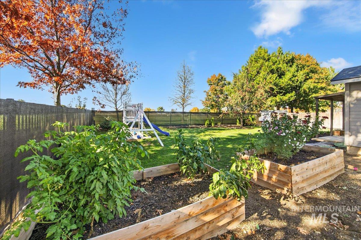 Fenced backyard featuring a vegetable garden and a playground
