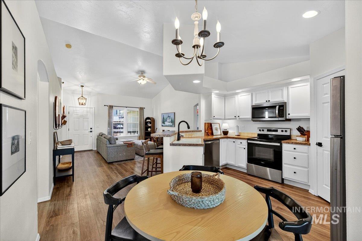 Kitchen with vaulted ceiling, white cabinets, stainless steel appliances, a peninsula, and decorative light fixtures