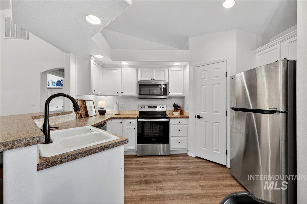 Kitchen featuring appliances with stainless steel finishes, white cabinets, light wood-style flooring, recessed lighting, and a peninsula