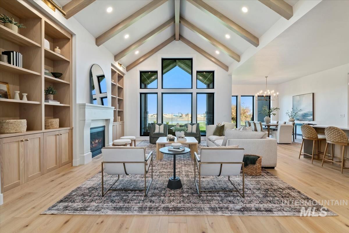 Living area with beam ceiling, healthy amount of natural light, a chandelier, a glass covered fireplace, and light wood-type flooring