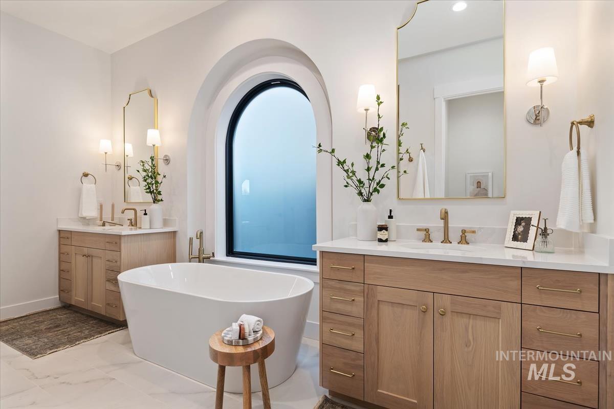 Bathroom with two vanities, a freestanding tub, and light marble finish floors