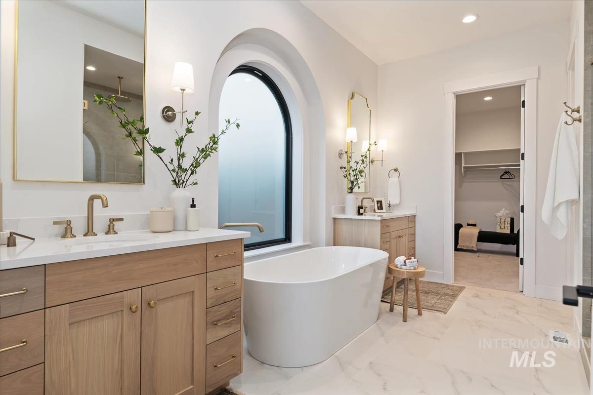 Bathroom with a spacious closet, two vanities, recessed lighting, light marble finish floors, and a stall shower