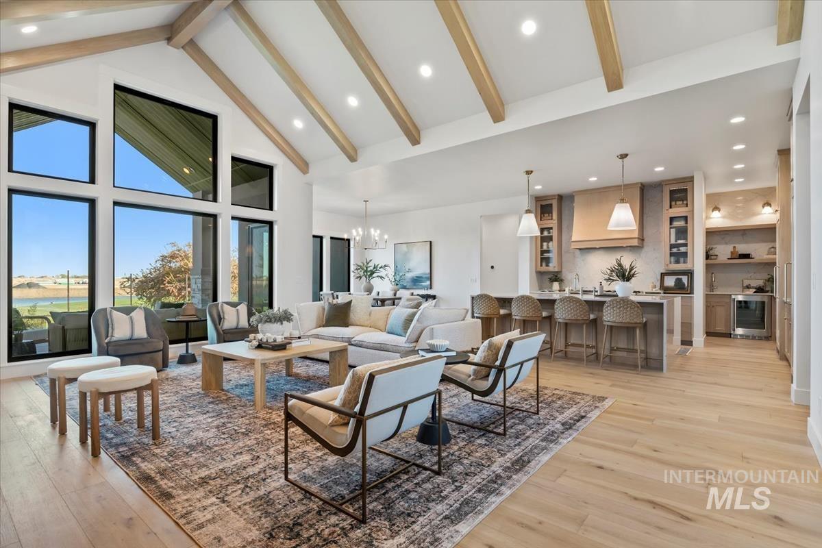Living area with beam ceiling, high vaulted ceiling, a chandelier, light wood-style floors, and beverage cooler