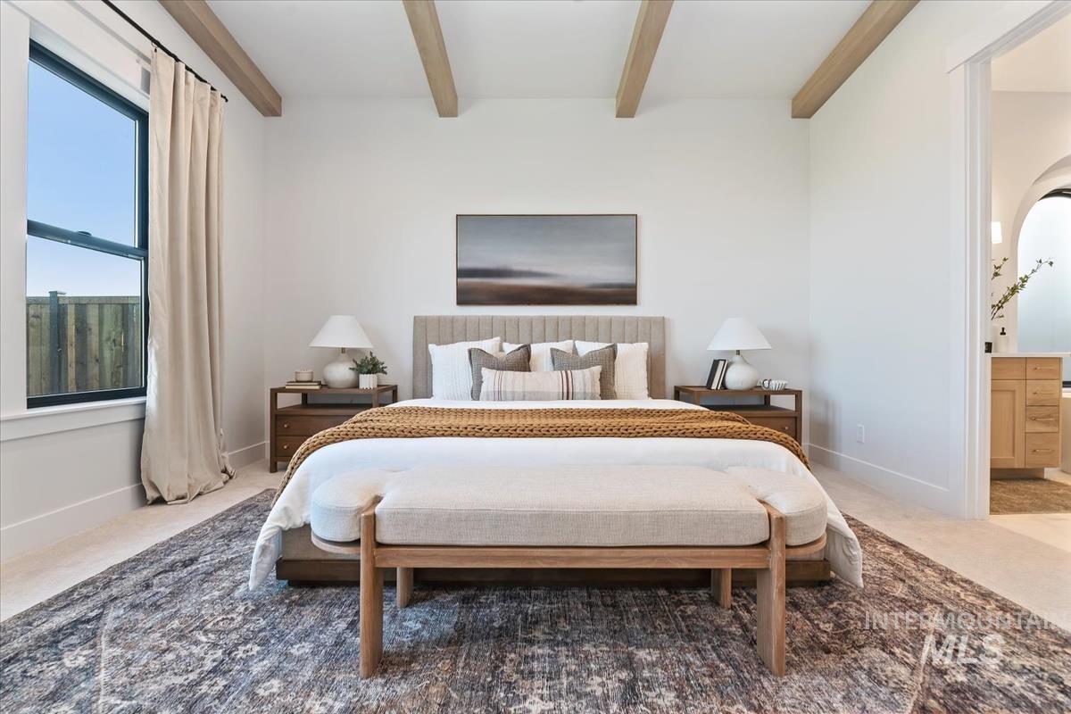 Carpeted bedroom with beamed ceiling, ensuite bath, and arched walkways