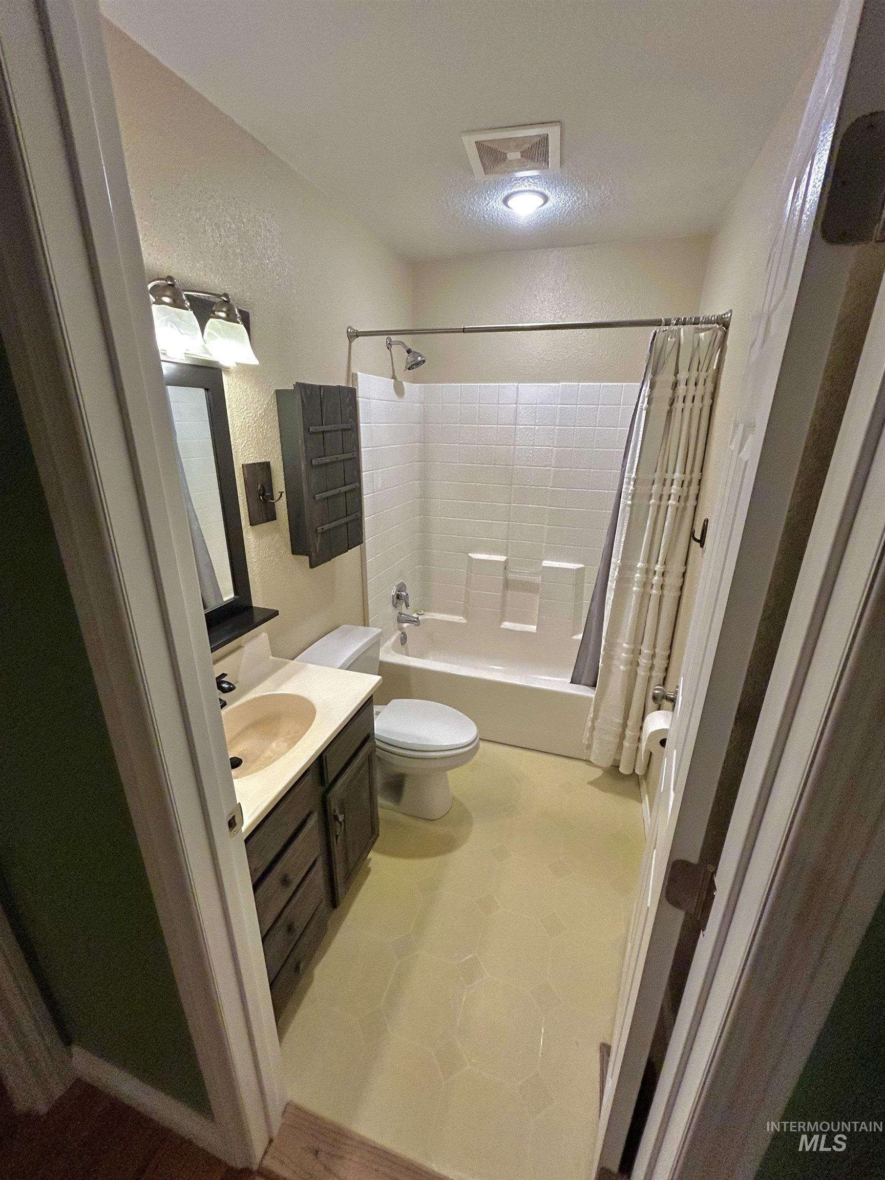 Full bath with vanity, a textured wall, and shower / bath combo
