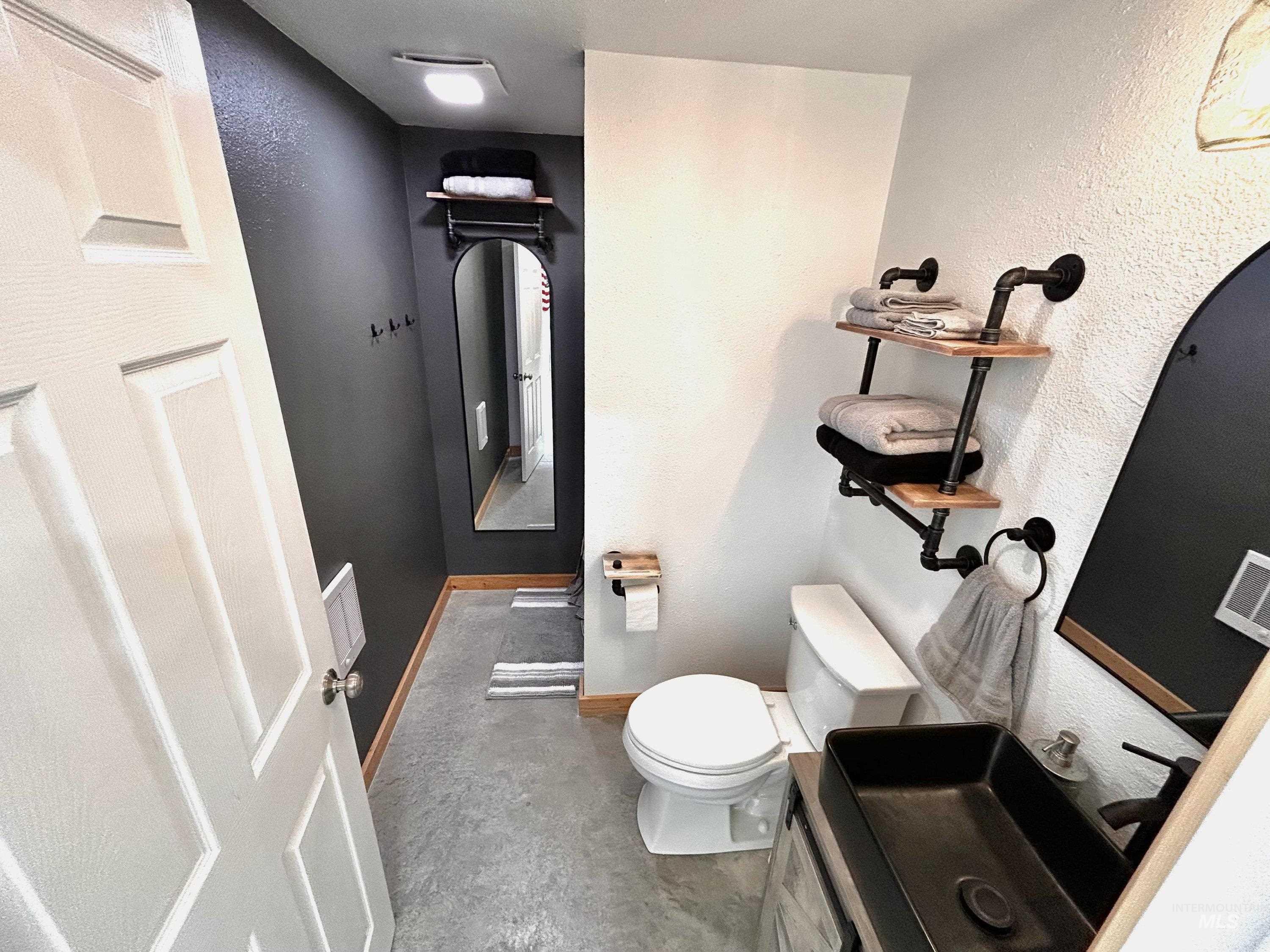 Half bathroom featuring a textured wall, vanity, and concrete flooring