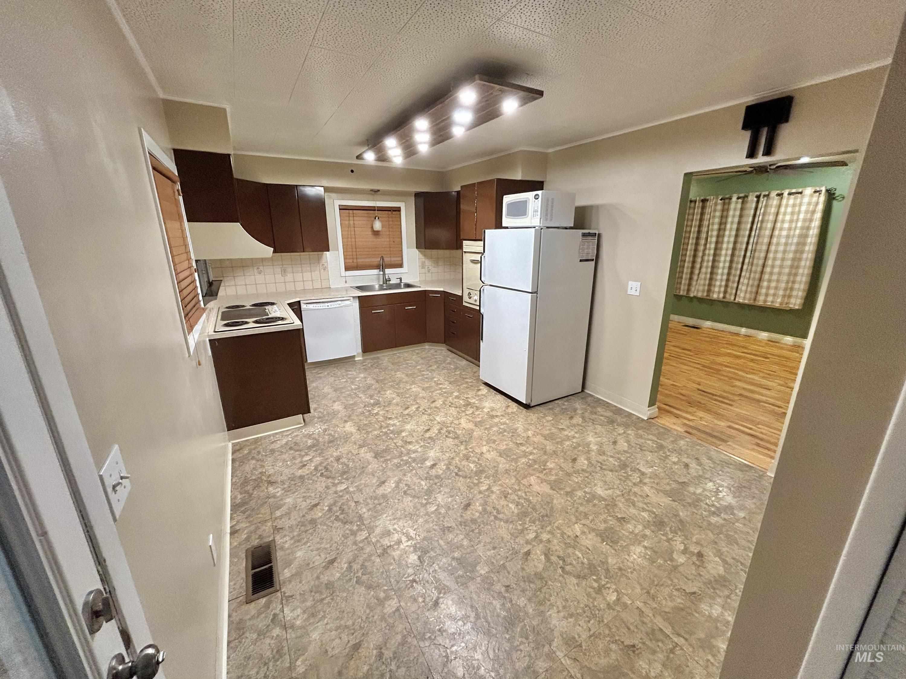 Kitchen featuring backsplash, white appliances, light countertops, a textured ceiling, and dark brown cabinetry
