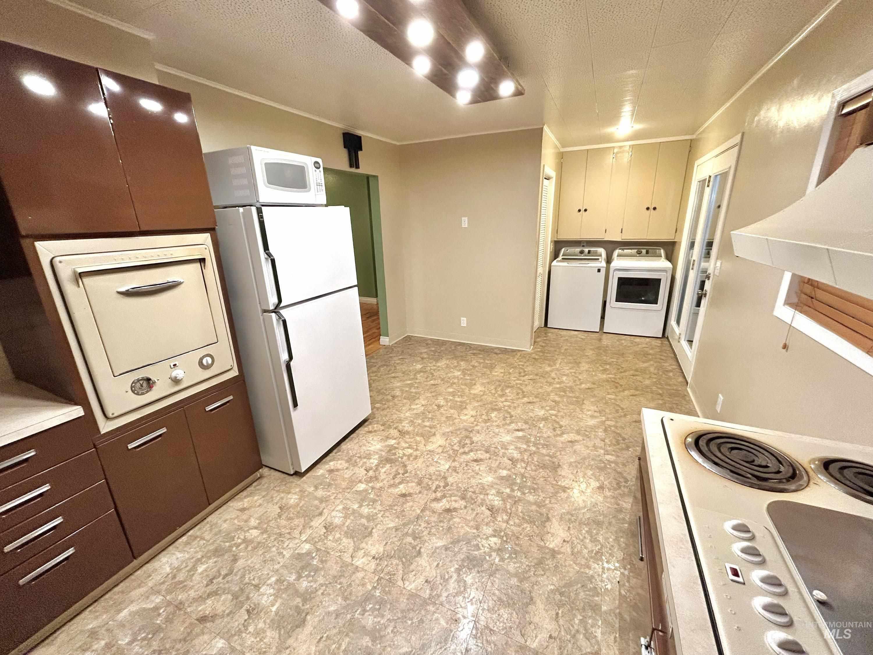 Kitchen featuring a textured ceiling, white appliances, independent washer and dryer, ornamental molding, and light countertops