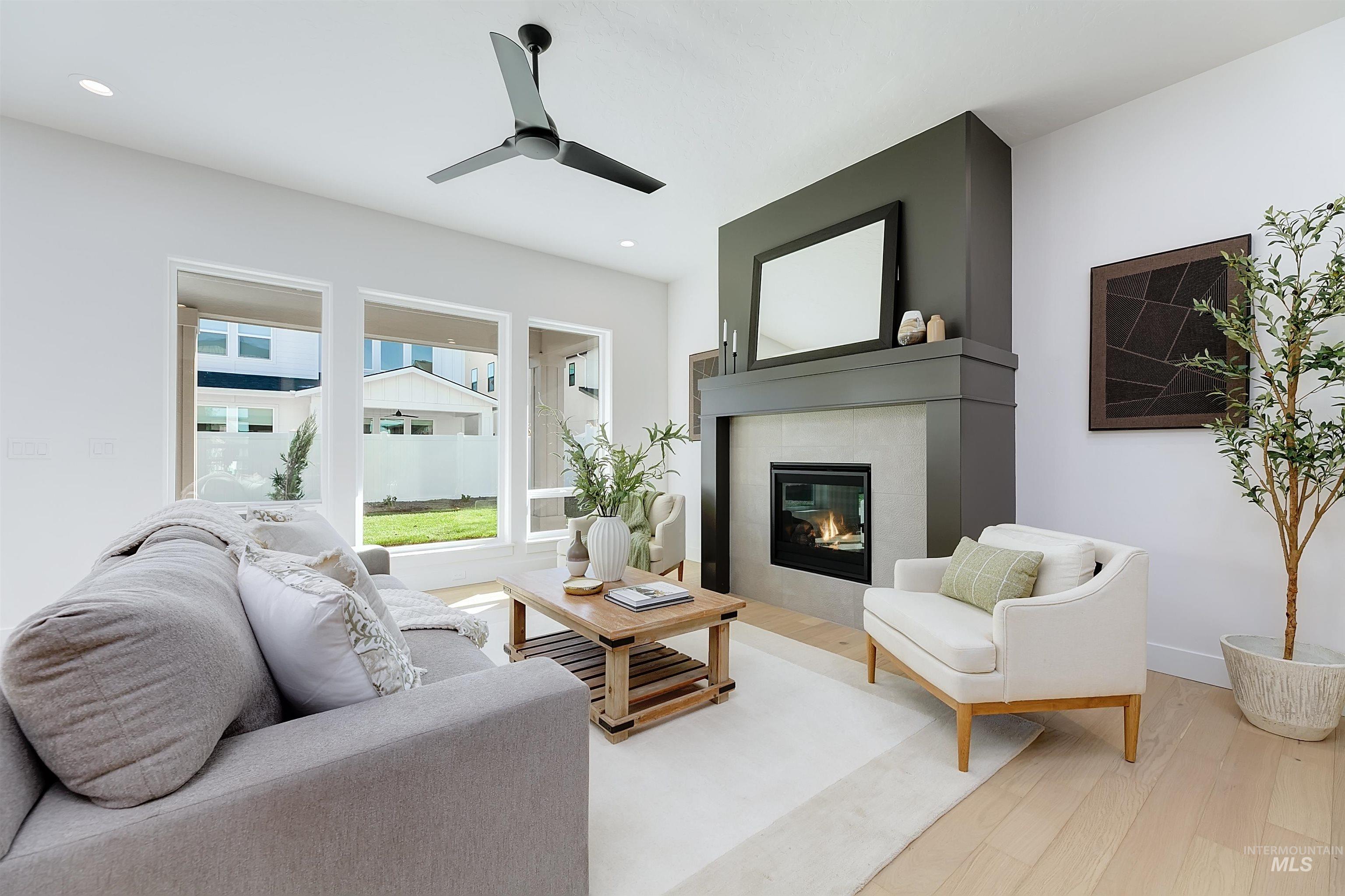 Living room featuring wood finished floors, a tiled fireplace, ceiling fan, and recessed lighting