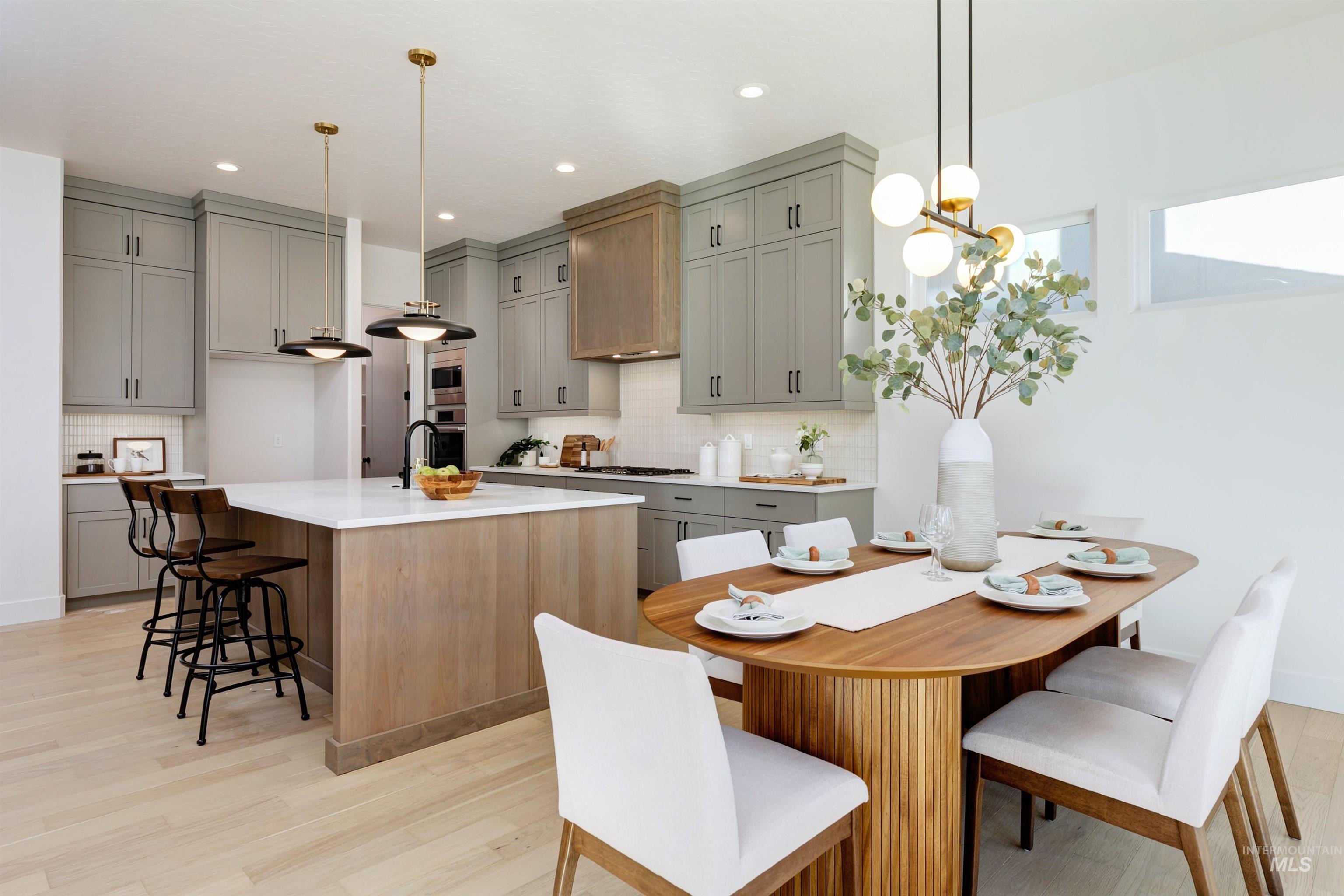 Kitchen featuring a kitchen breakfast bar, an island with sink, pendant lighting, gray cabinets, and light wood finished floors