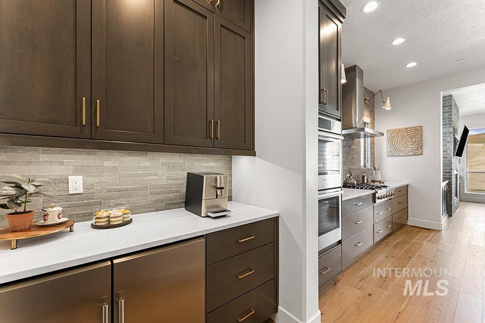 Kitchen featuring wall chimney exhaust hood, tasteful backsplash, light wood finished floors, light countertops, and recessed lighting