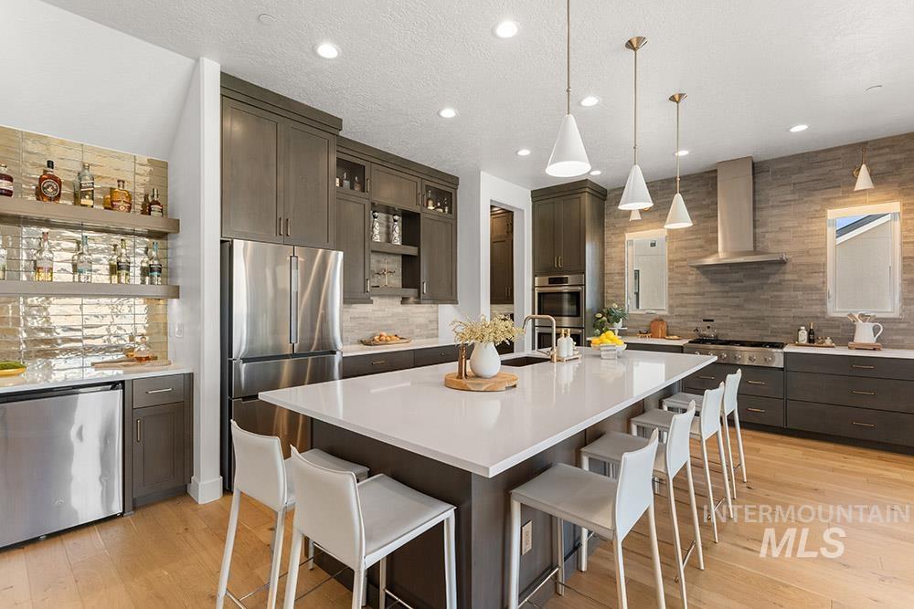 Kitchen with wall chimney range hood, stainless steel appliances, open shelves, backsplash, and a breakfast bar