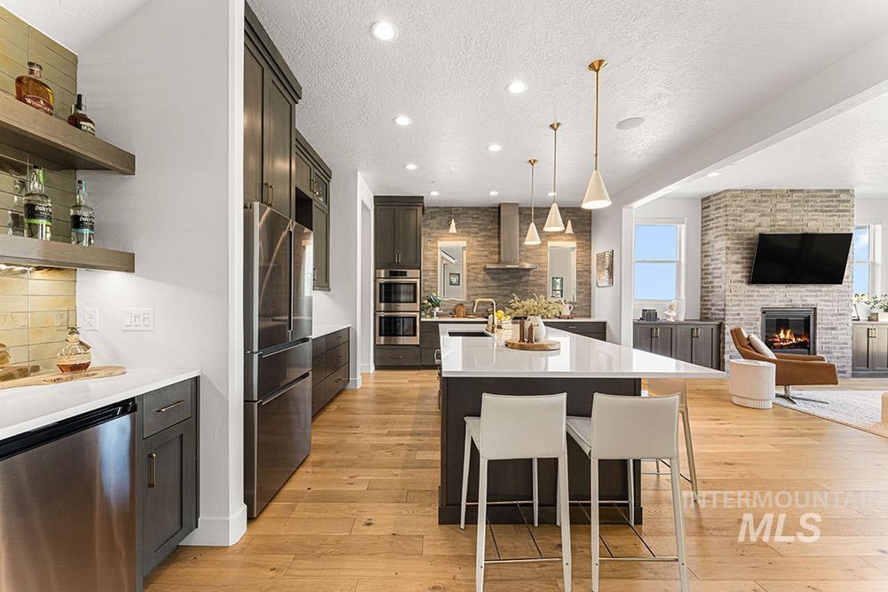 Kitchen with stainless steel appliances, wall chimney exhaust hood, open floor plan, a kitchen island with sink, and a brick fireplace