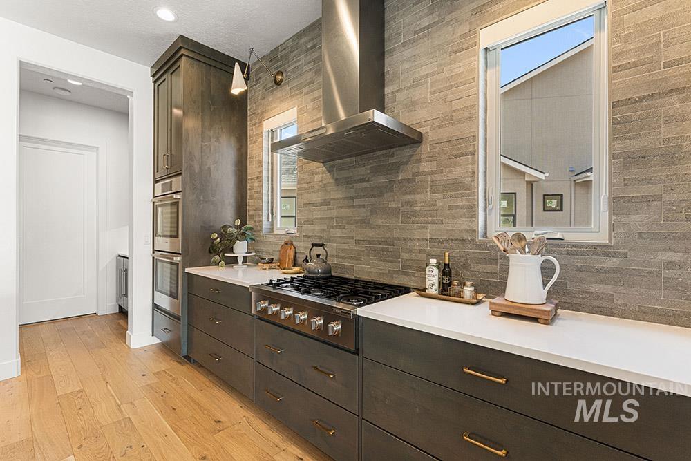 Kitchen featuring wall chimney exhaust hood, appliances with stainless steel finishes, backsplash, light wood-style flooring, and light countertops