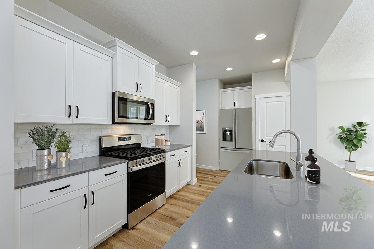 Kitchen with stainless steel appliances, light wood-style floors, recessed lighting, white cabinets, and backsplash