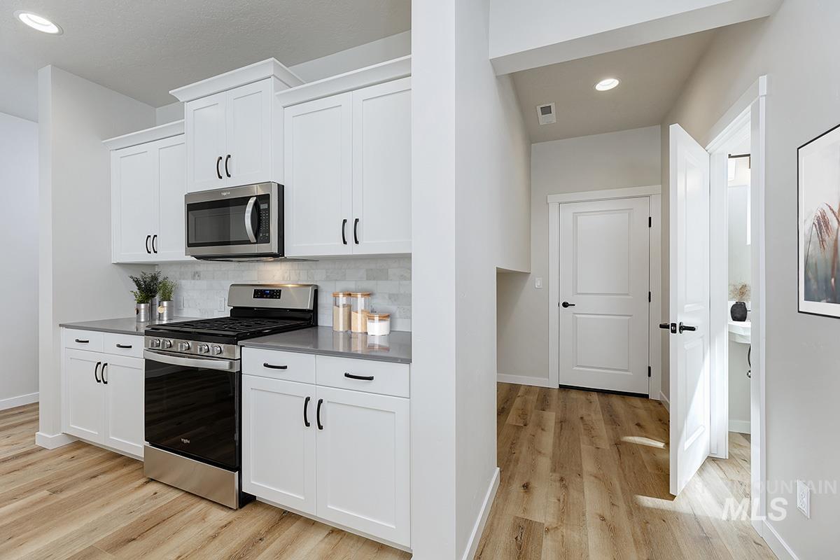 Kitchen featuring appliances with stainless steel finishes, recessed lighting, light wood-style floors, white cabinets, and backsplash