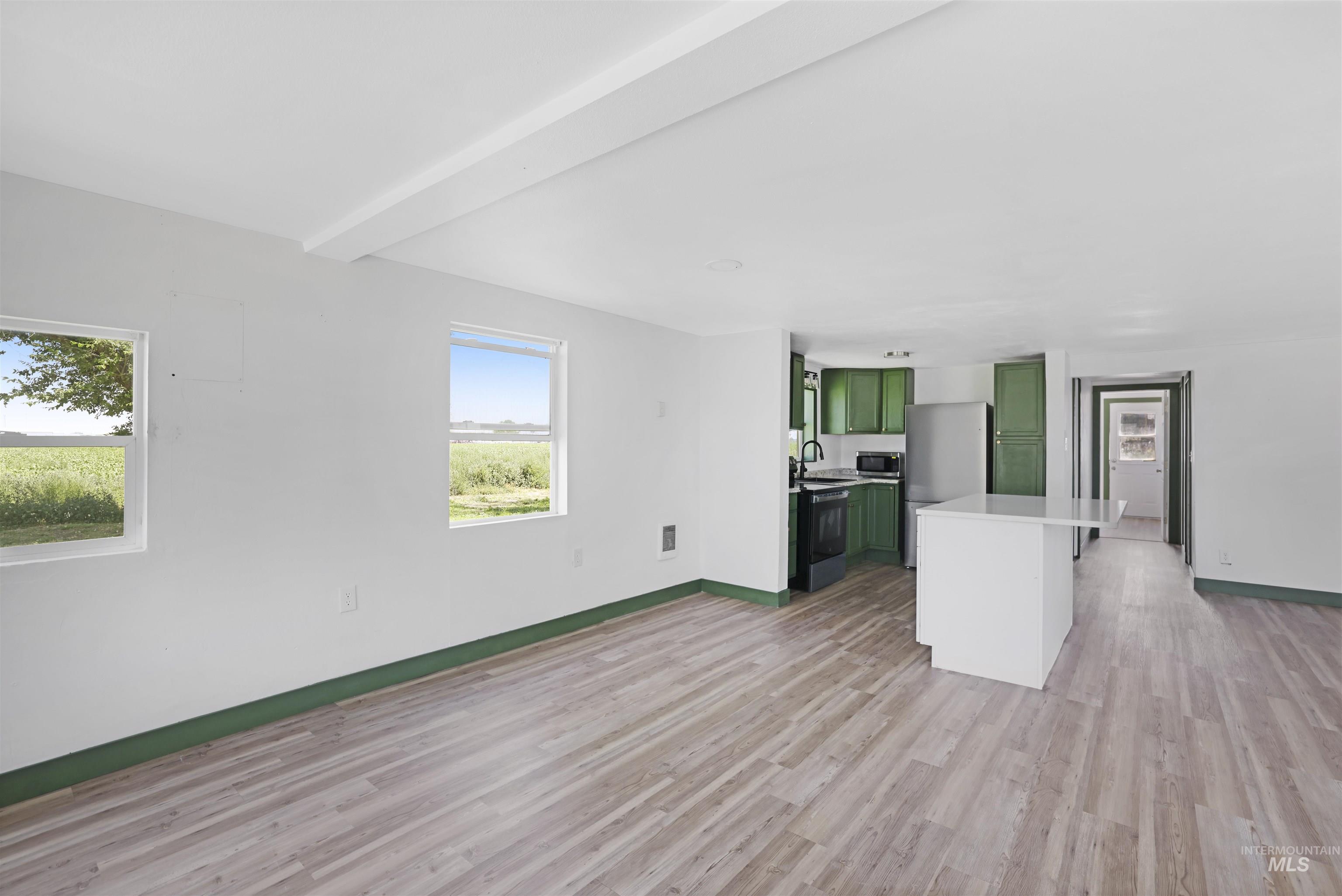 Kitchen featuring green cabinets, light wood-style flooring, light countertops, beam ceiling, and appliances with stainless steel finishes