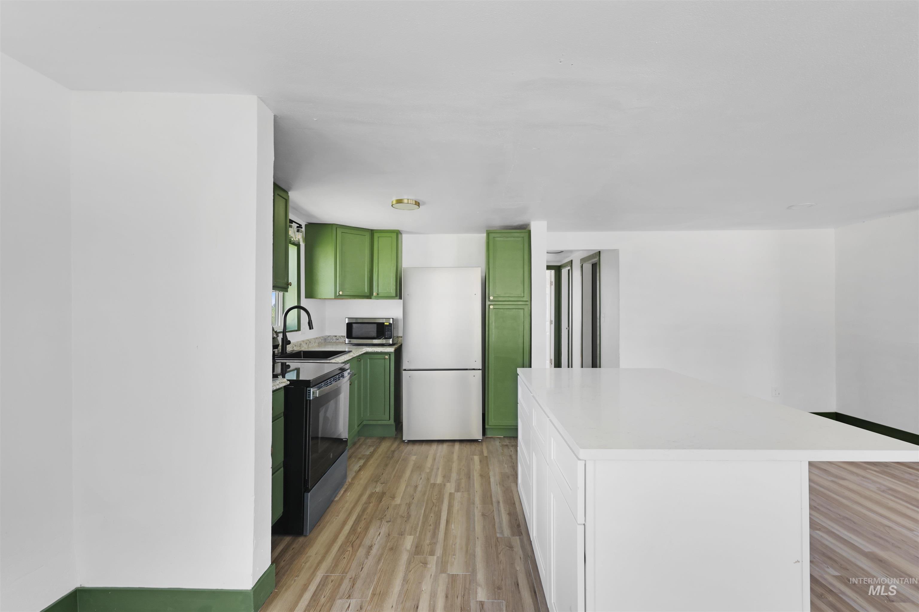 Kitchen featuring green cabinets, appliances with stainless steel finishes, light wood-style flooring, a kitchen island, and white cabinets