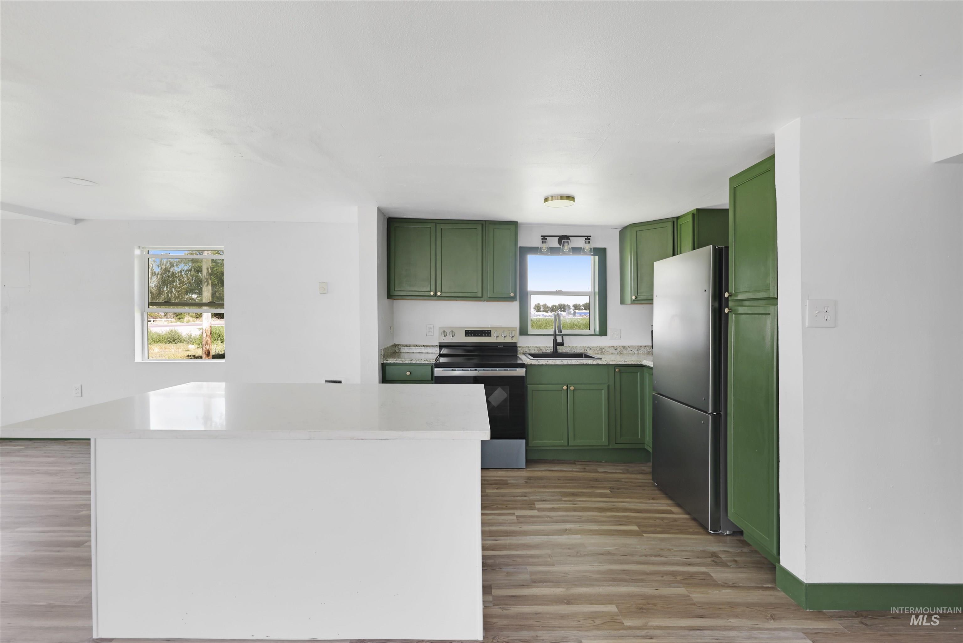 Kitchen featuring green cabinets, stainless steel appliances, a kitchen island, light wood-style flooring, and light stone countertops