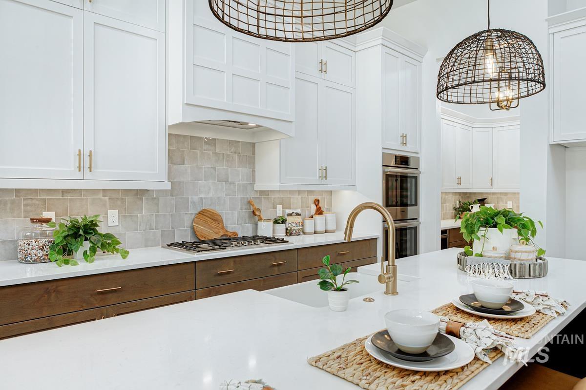 Kitchen featuring decorative backsplash, white cabinets, stainless steel appliances, light stone countertops, and decorative light fixtures
