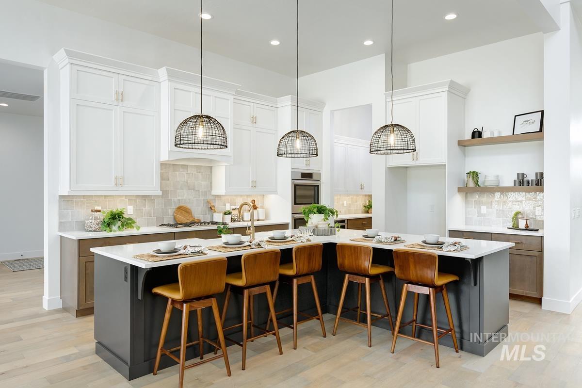 Kitchen with a kitchen breakfast bar, decorative backsplash, a large island with sink, white cabinets, and recessed lighting