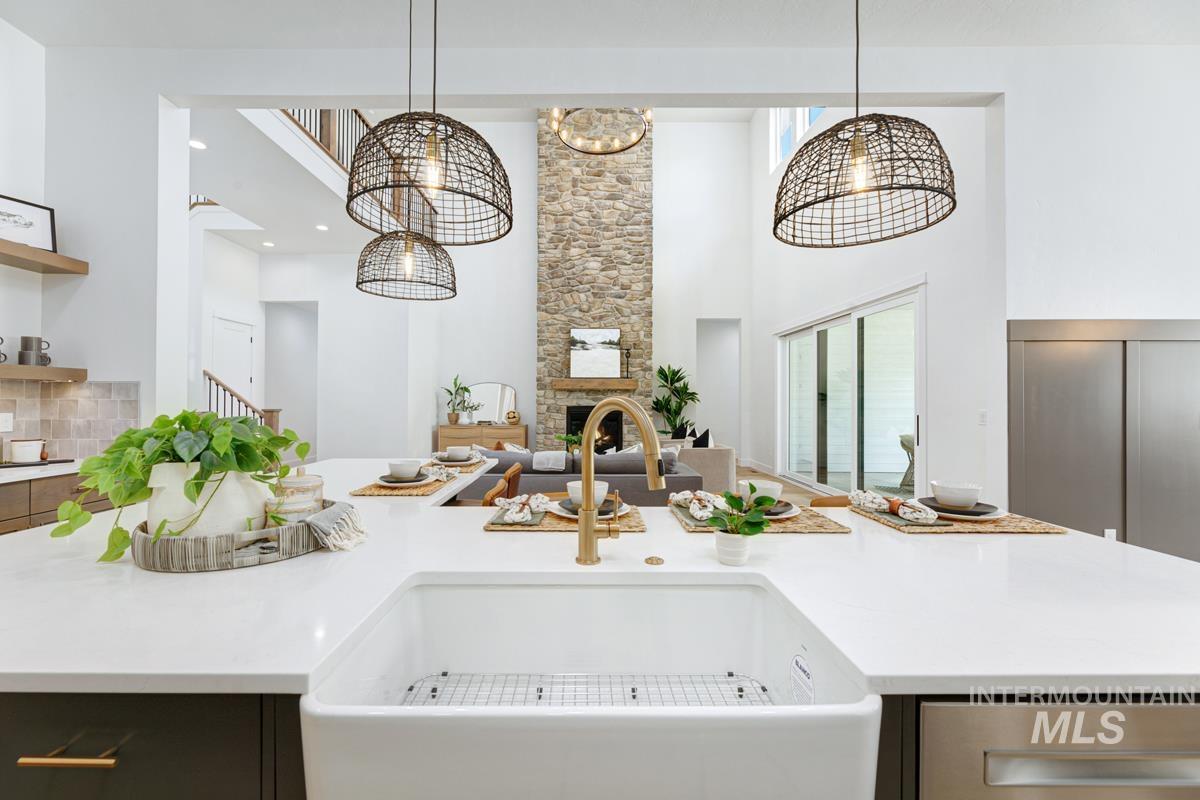 Kitchen featuring a center island with sink, a high ceiling, light stone counters, decorative light fixtures, and open floor plan