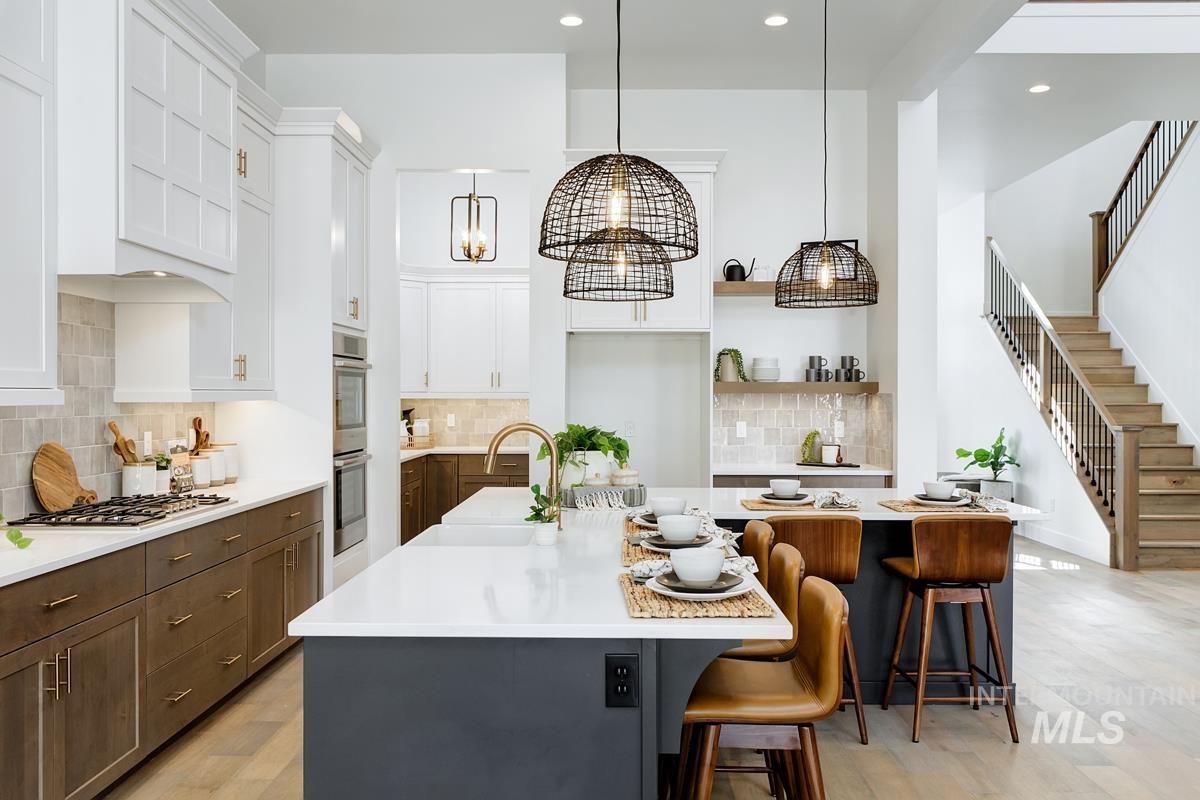 Kitchen featuring tasteful backsplash, a center island with sink, a kitchen bar, hanging light fixtures, and light wood-type flooring