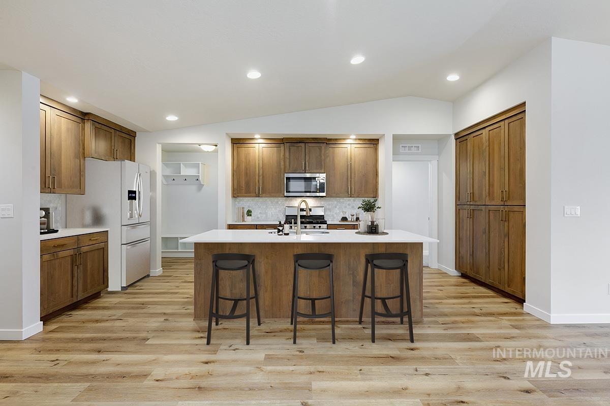 Kitchen with decorative backsplash, lofted ceiling, a kitchen bar, brown cabinets, and light wood finished floors