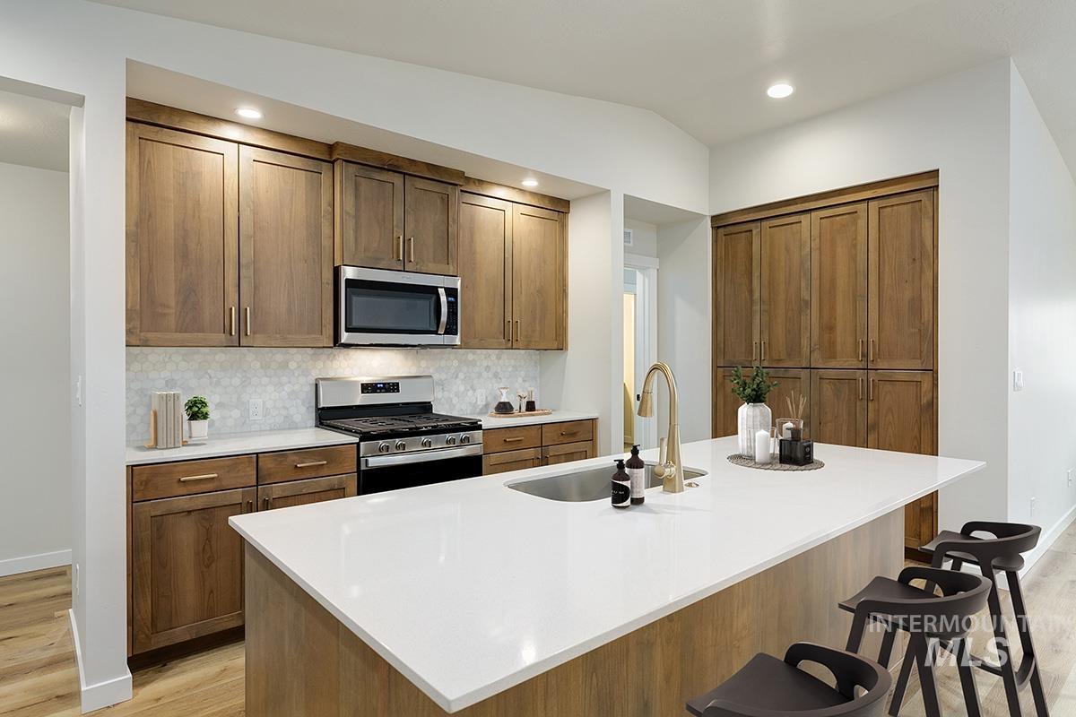 Kitchen featuring appliances with stainless steel finishes, a breakfast bar, light wood-type flooring, tasteful backsplash, and lofted ceiling
