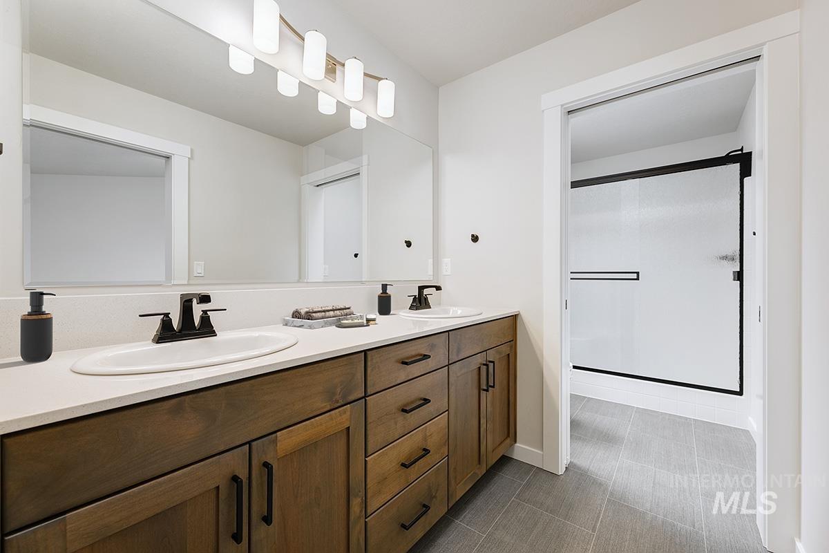 Full bathroom featuring double vanity, a stall shower, and dark tile patterned floors