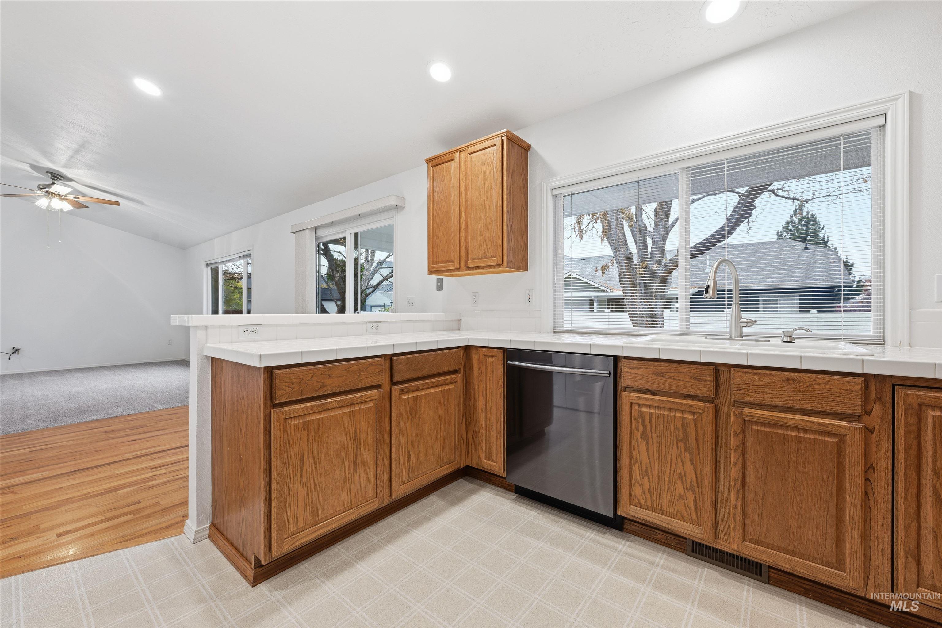 Kitchen with brown cabinetry, tile countertops, recessed lighting, stainless steel dishwasher, and a peninsula