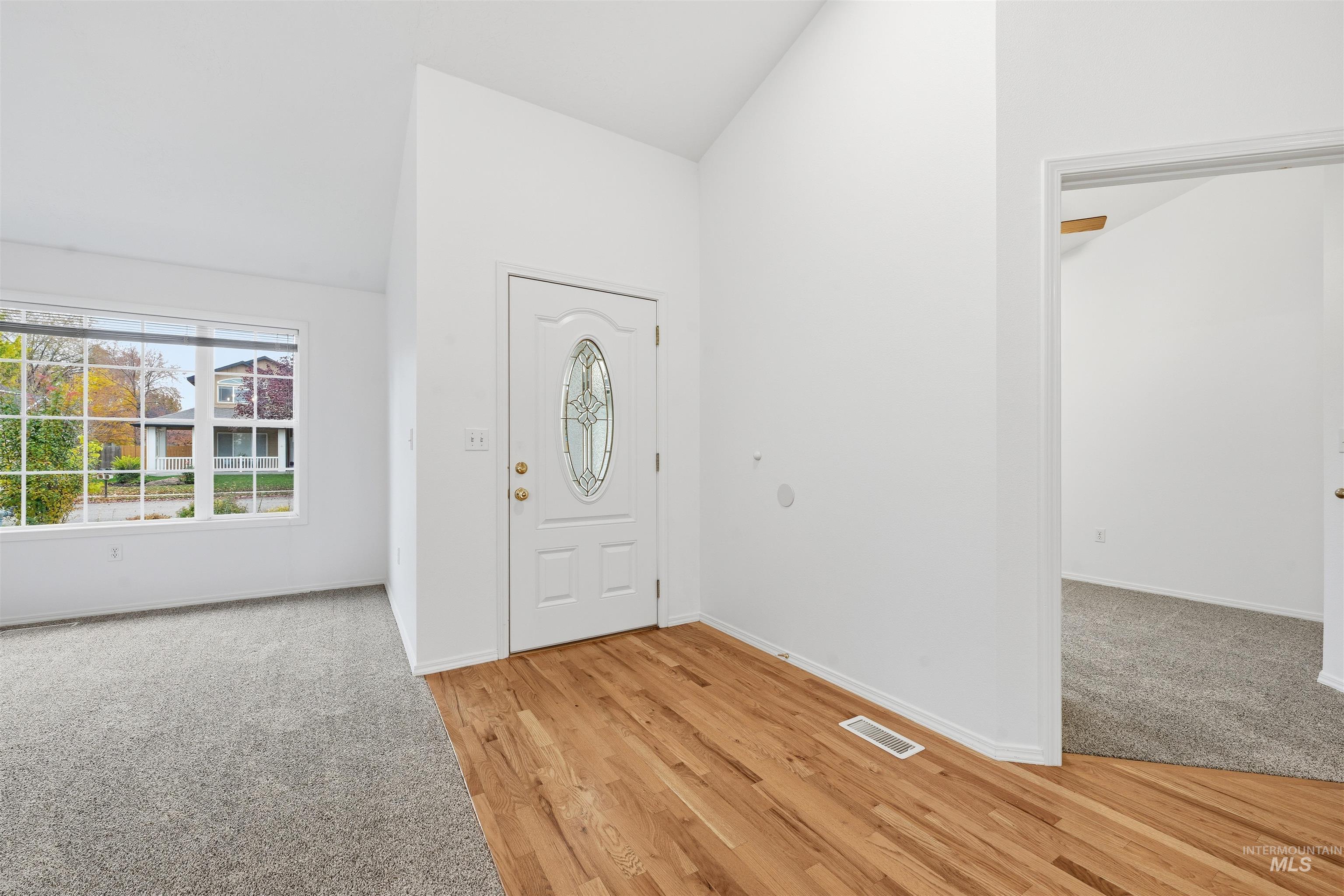 Foyer entrance with lofted ceiling, light wood-style flooring, and light colored carpet
