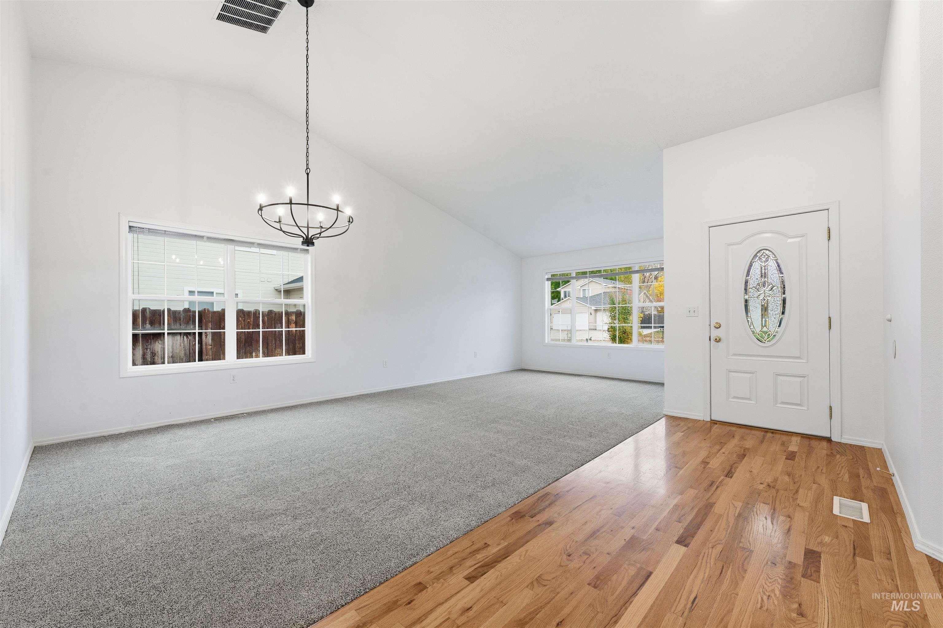 Foyer entrance with high vaulted ceiling, light wood-type flooring, a chandelier, and light colored carpet