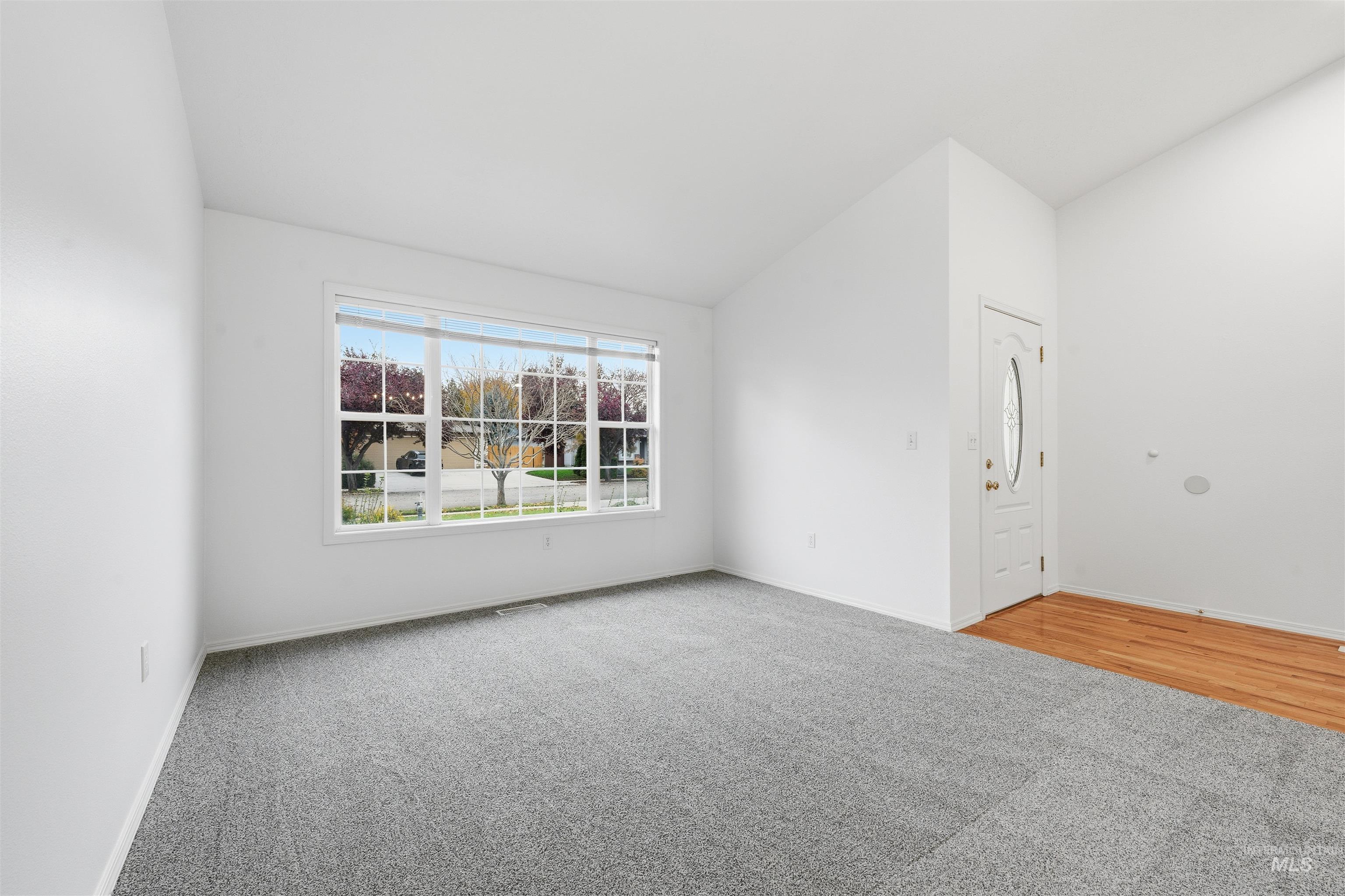 Unfurnished room featuring light carpet and lofted ceiling