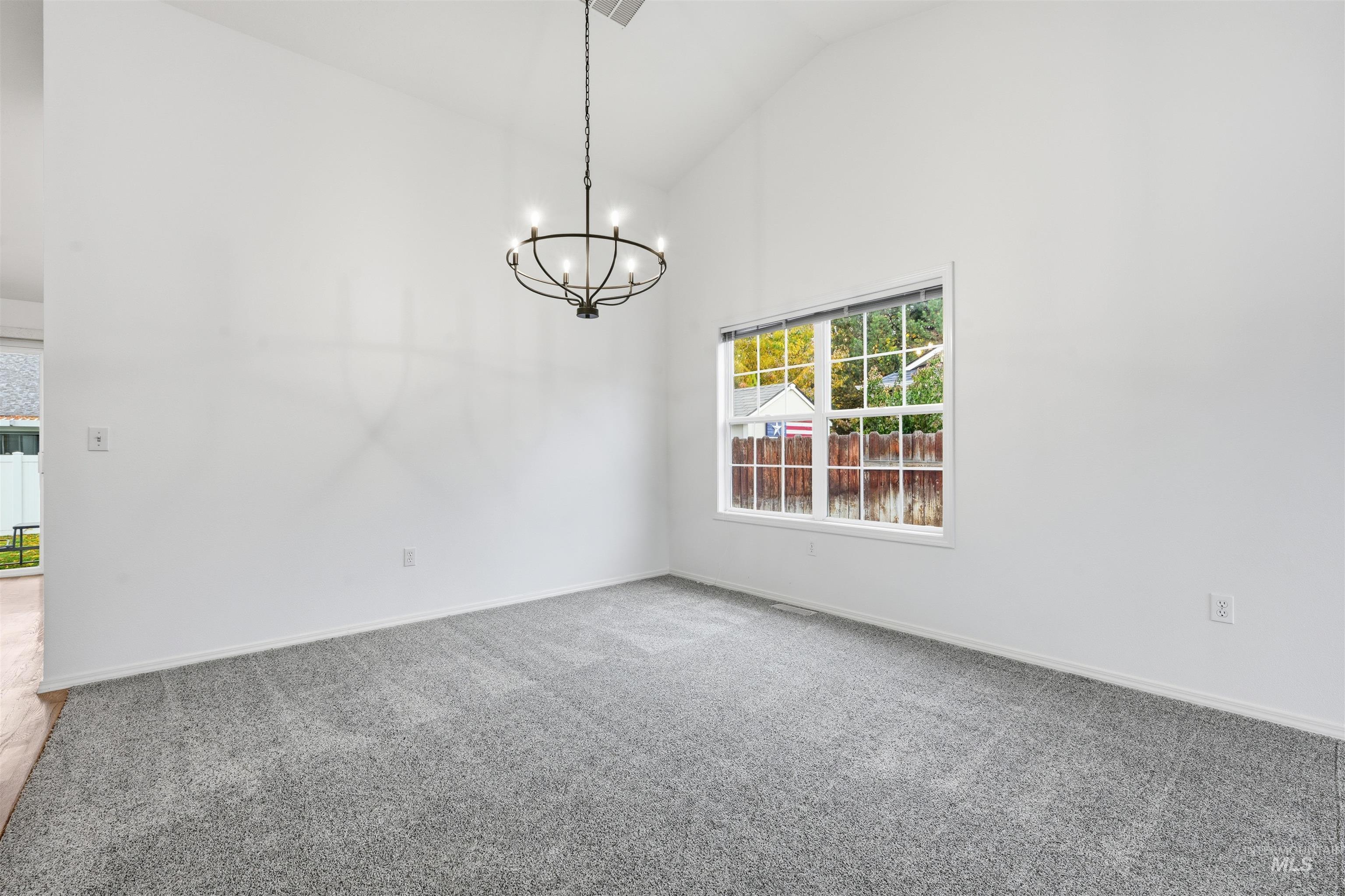 Empty room with carpet flooring, a chandelier, and high vaulted ceiling