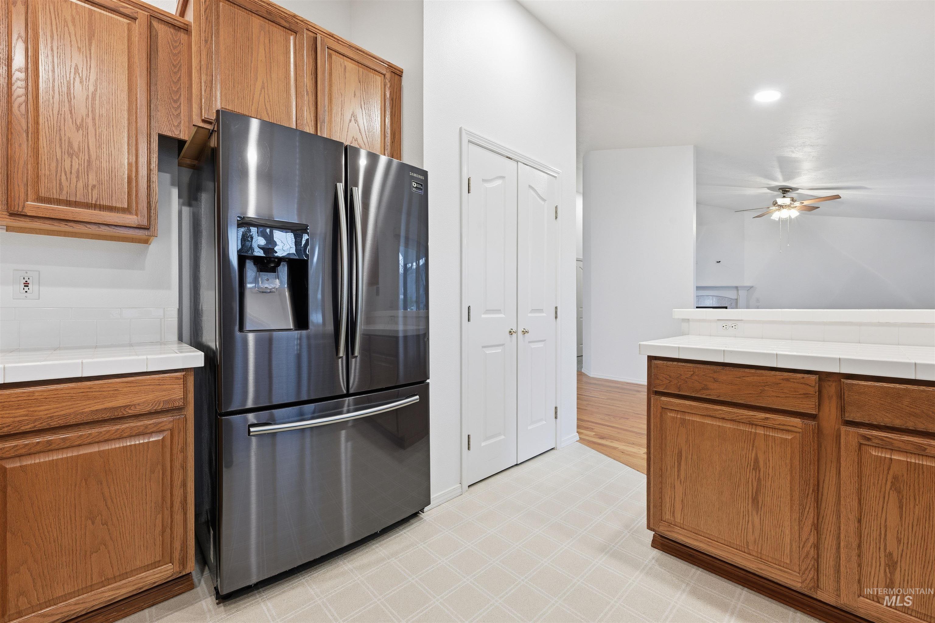 Kitchen featuring tile countertops, brown cabinets, stainless steel refrigerator with ice dispenser, a ceiling fan, and recessed lighting